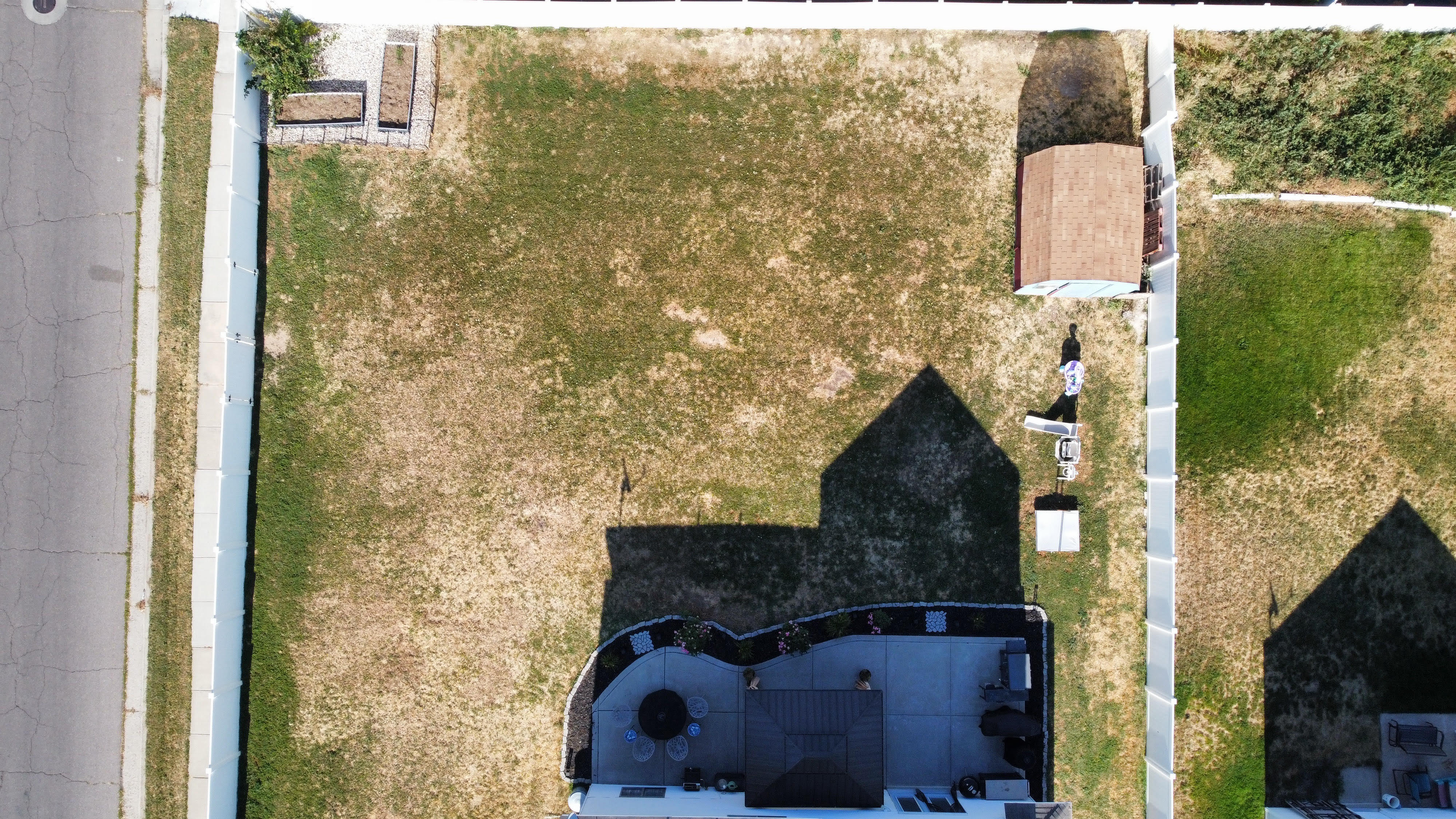 Expansive lot featuring a detached shed, paved sidewalk, and a concrete patio with a built-in fire pit