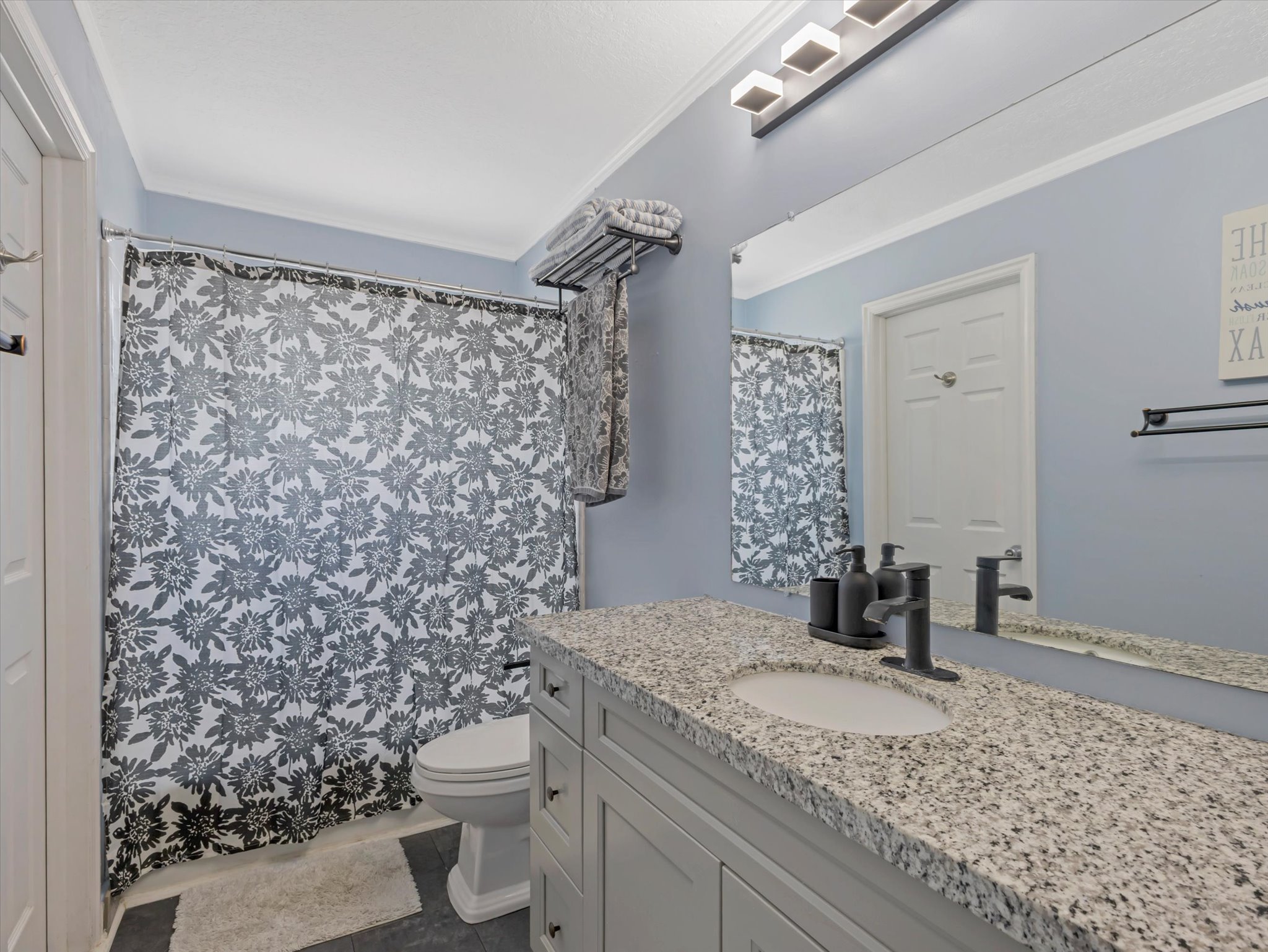 Bathroom featuring a single vanity with stone countertop and integrated sink, matte black faucet, and a large wall-mounted mirror with overhead lighting