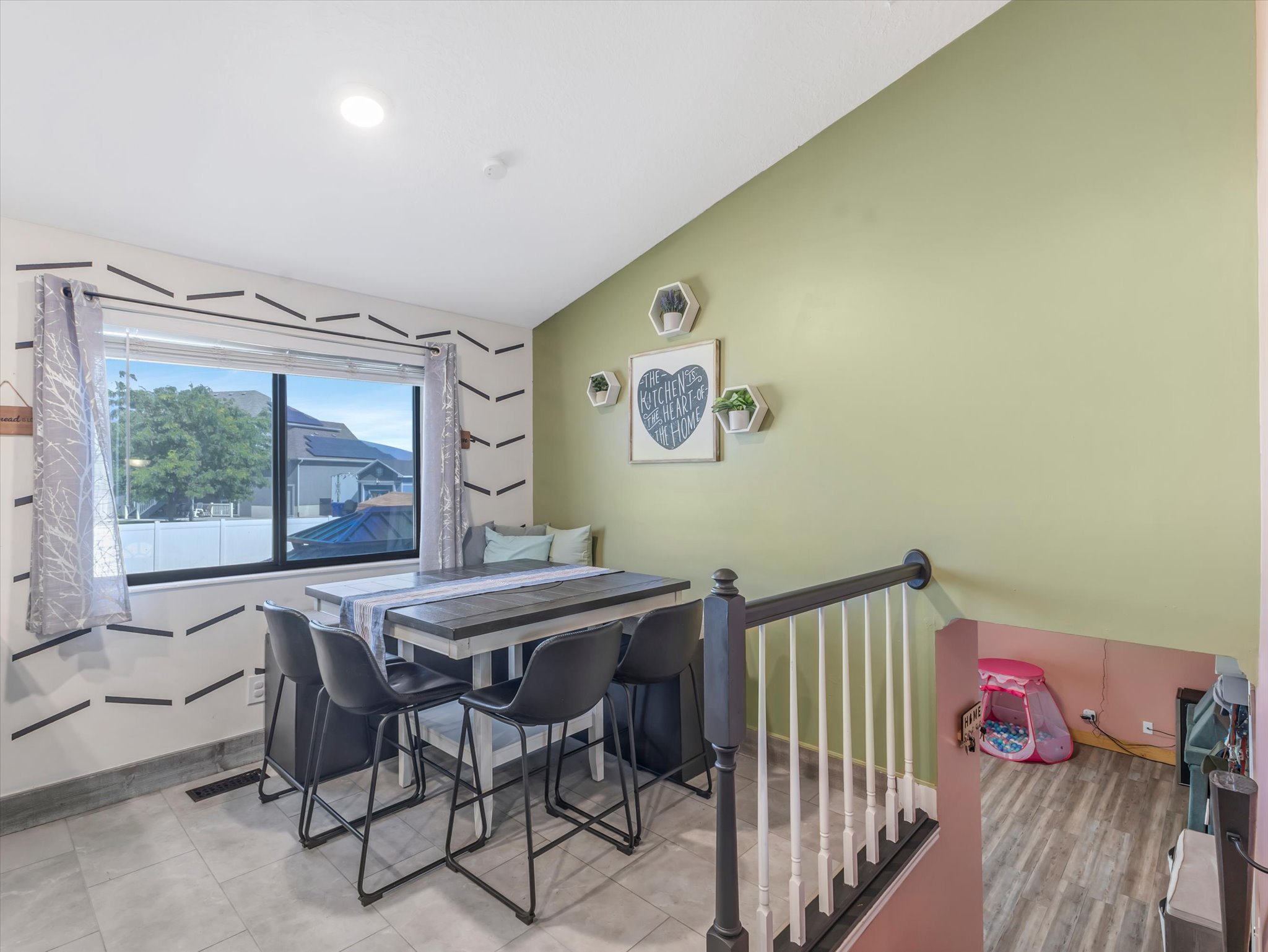 Dining area featuring contemporary light green wall, large window with outdoor views, light tile flooring, and a built-in bench seating area