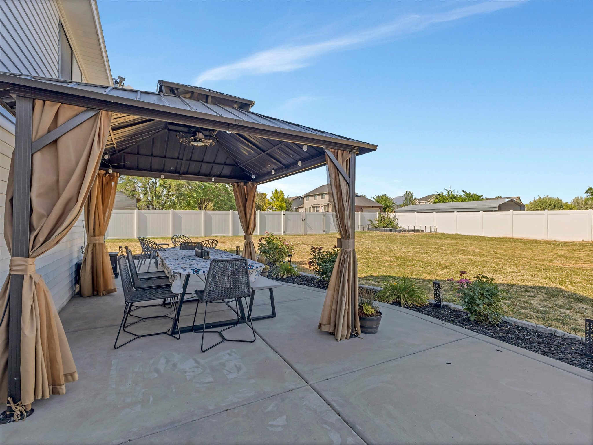 Concrete patio with a dark metal gazebo featuring privacy curtains, string lighting, and a vented roof