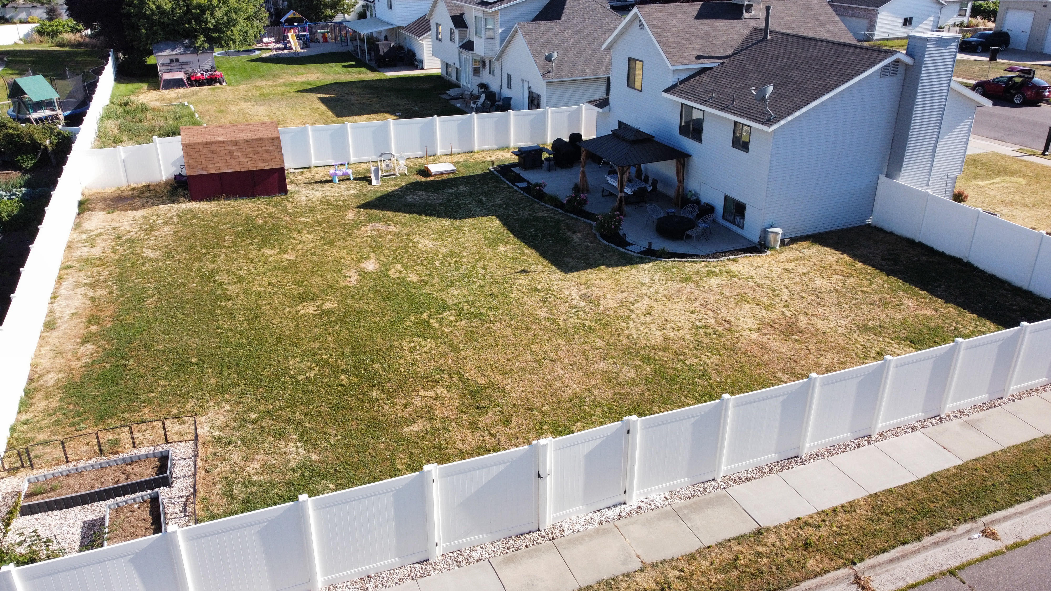Expansive backyard featuring a white privacy fence, an elevated patio with a pergola, a storage shed, and raised garden beds