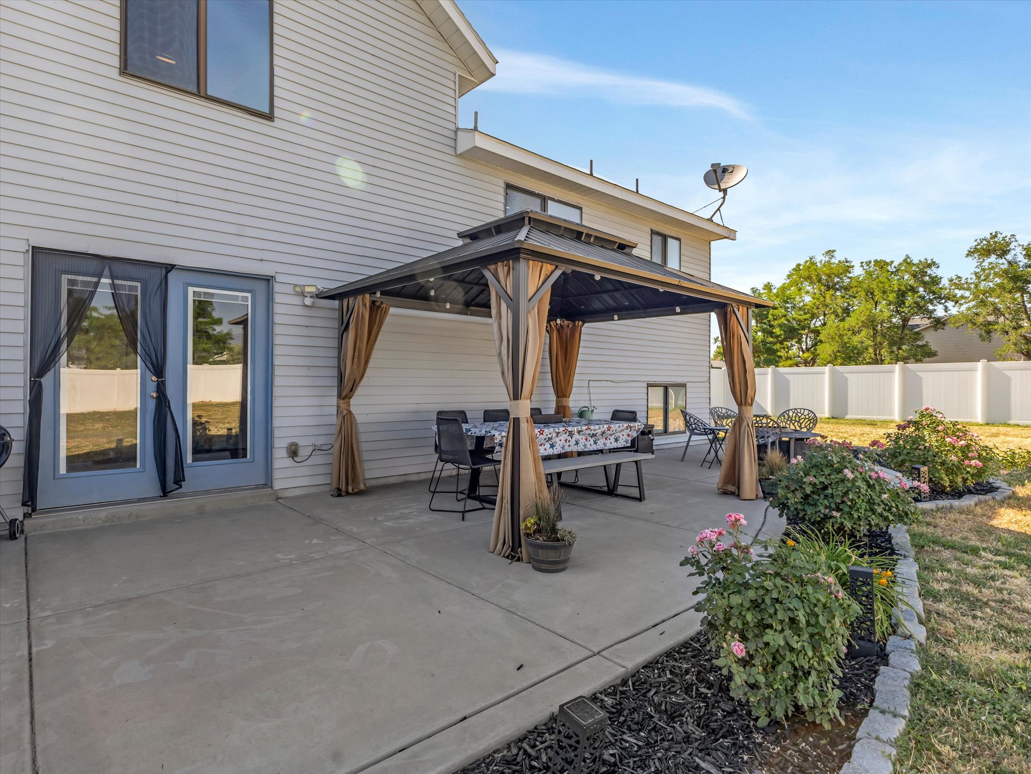 Spacious concrete patio featuring a gazebo, direct access via patio doors, and surrounding planted garden beds