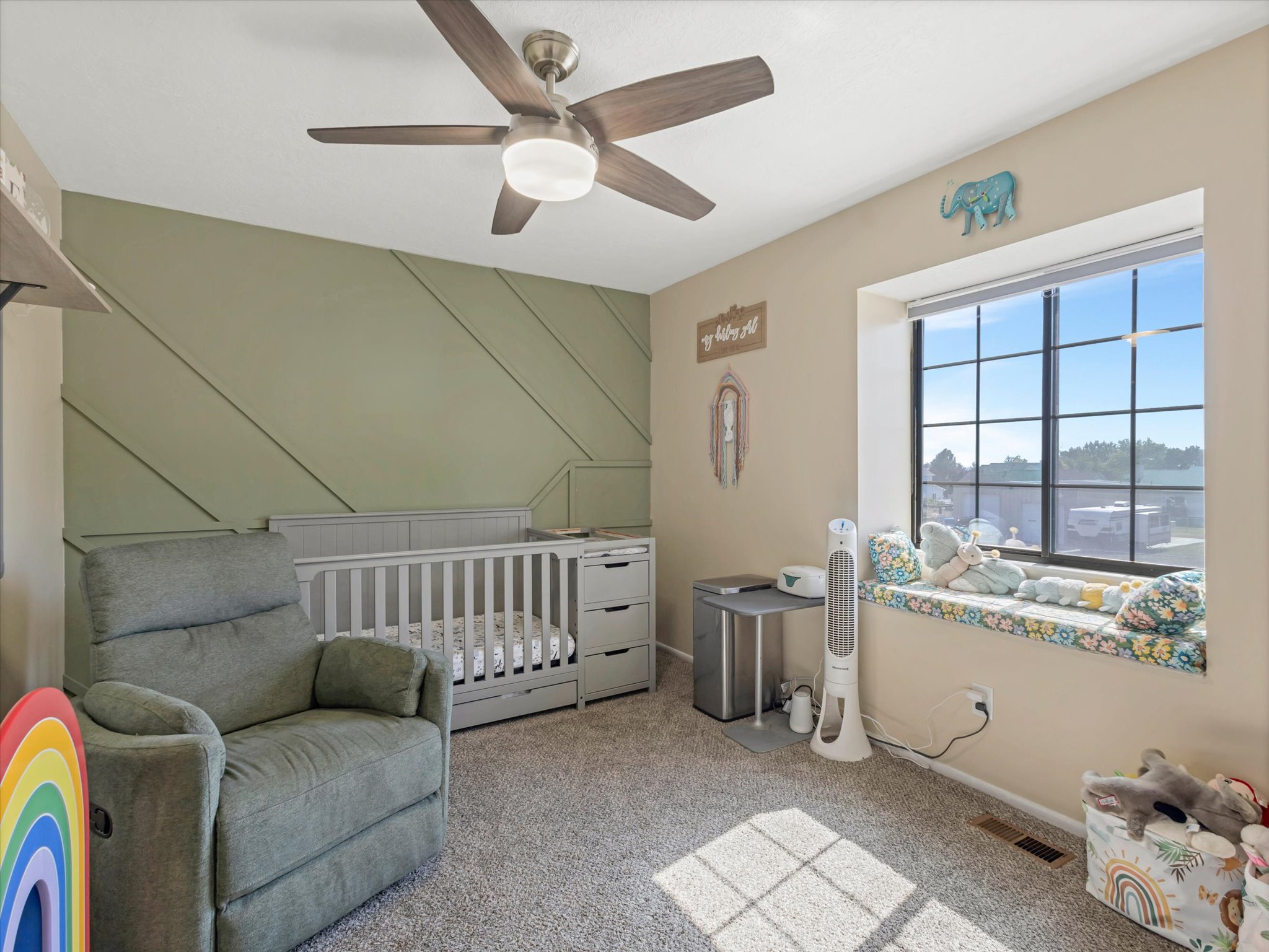 Windowed room featuring a ceiling fan, accent wall with diagonal wood trim, and a built-in window seat