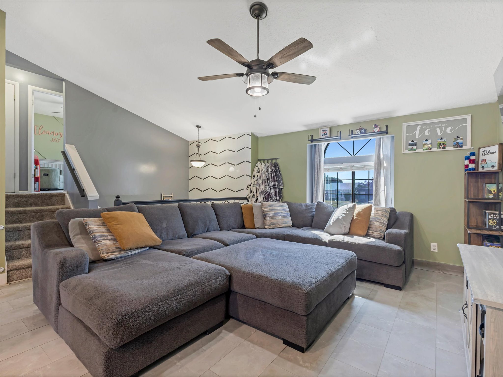 Vaulted ceiling living area featuring tile flooring, a contemporary ceiling fan with integrated lighting, and a prominent arched window