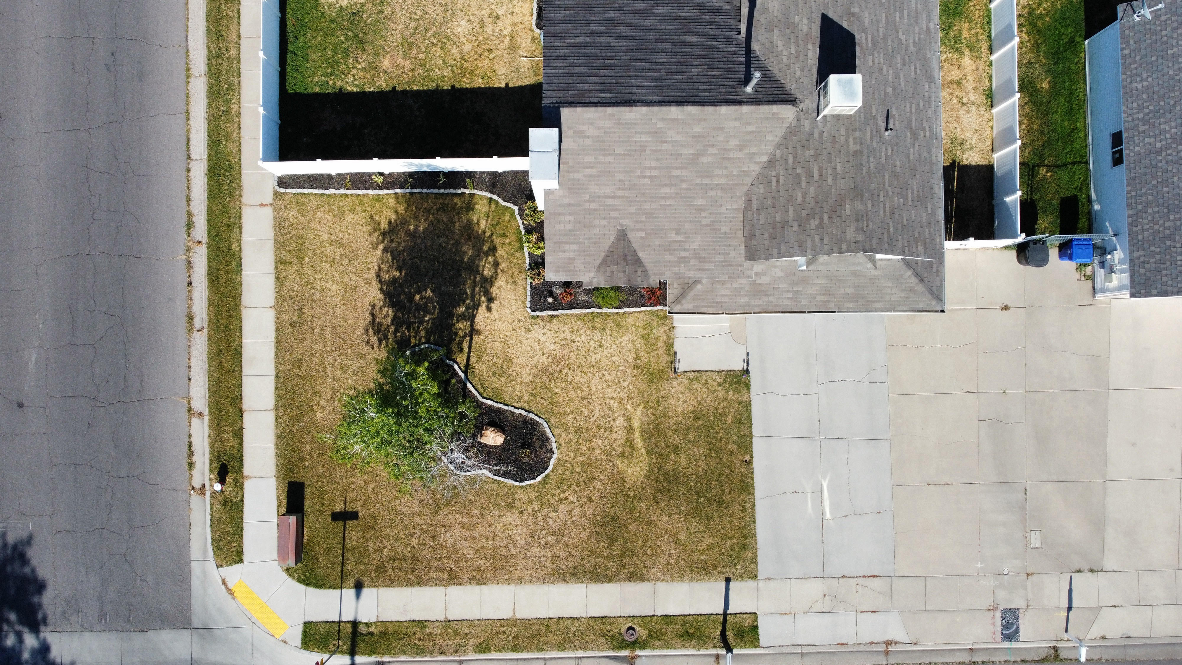 Corner lot property featuring a shingled roof, paved driveway, concrete sidewalks, and a fenced backyard
