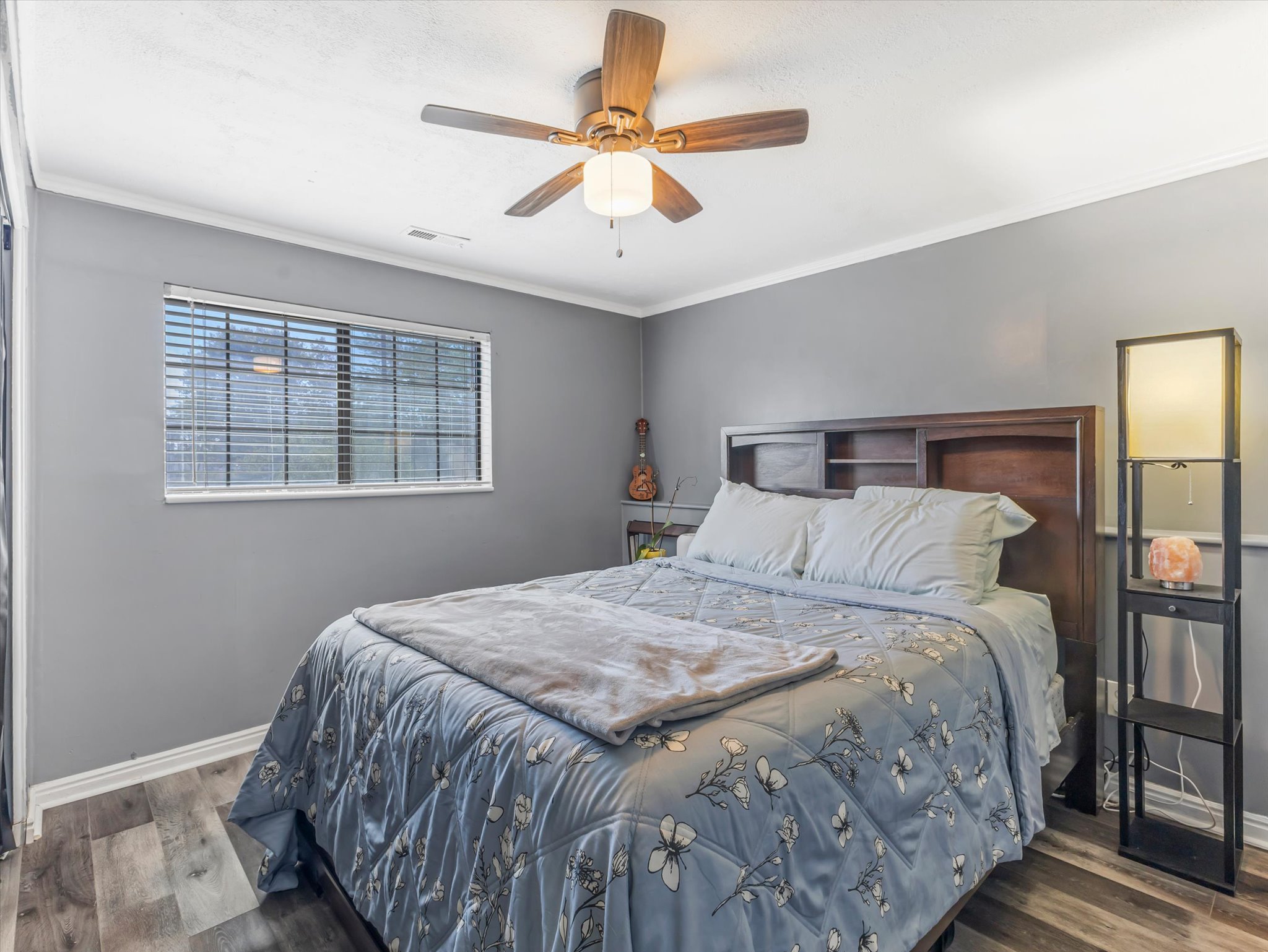Bedroom featuring wood-finish flooring, a ceiling fan with integrated lighting, and a window with horizontal blinds