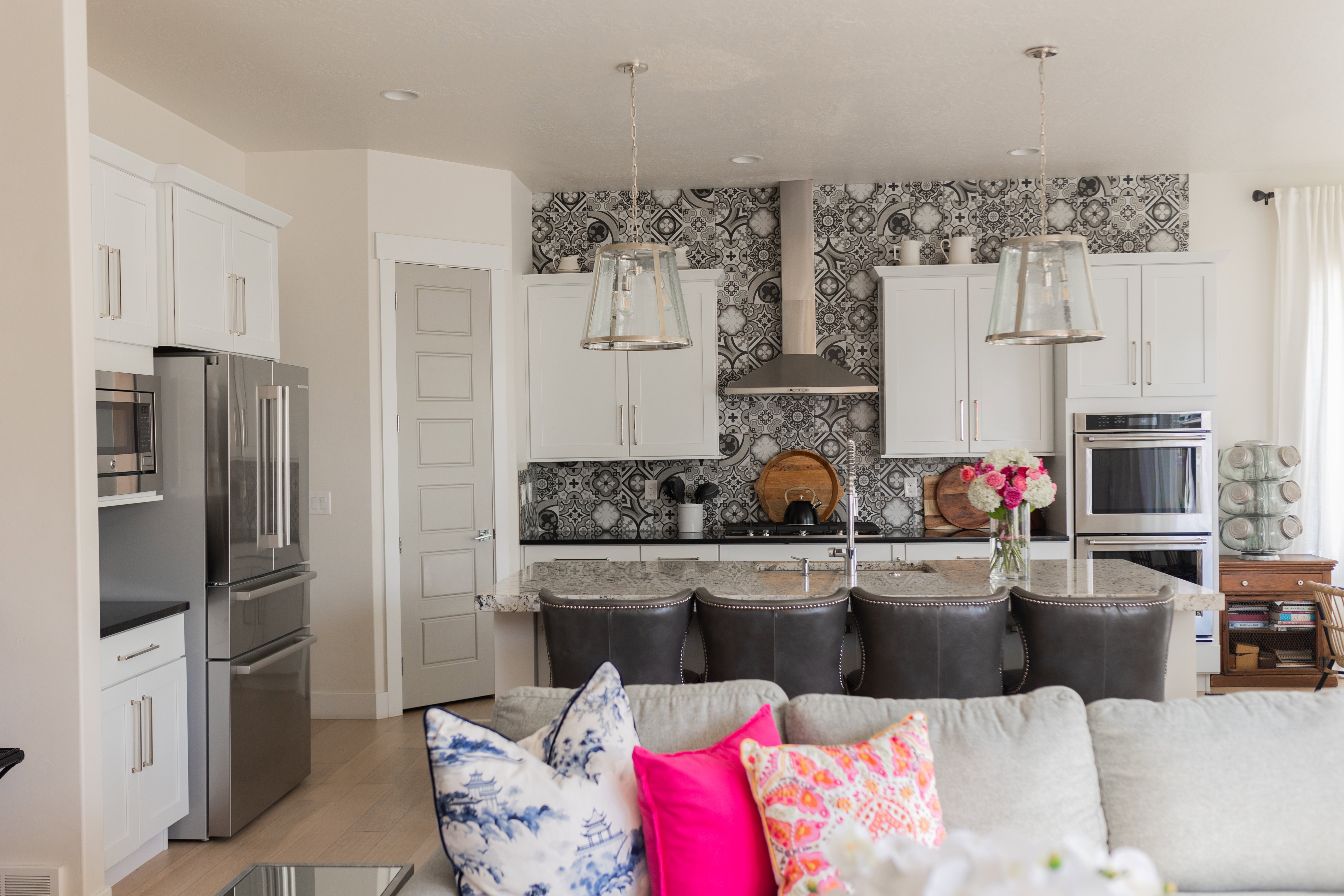 Contemporary kitchen featuring white cabinetry, stainless steel appliances, a patterned tile backsplash, an eat-at island with granite-finish countertop, and pendant lighting