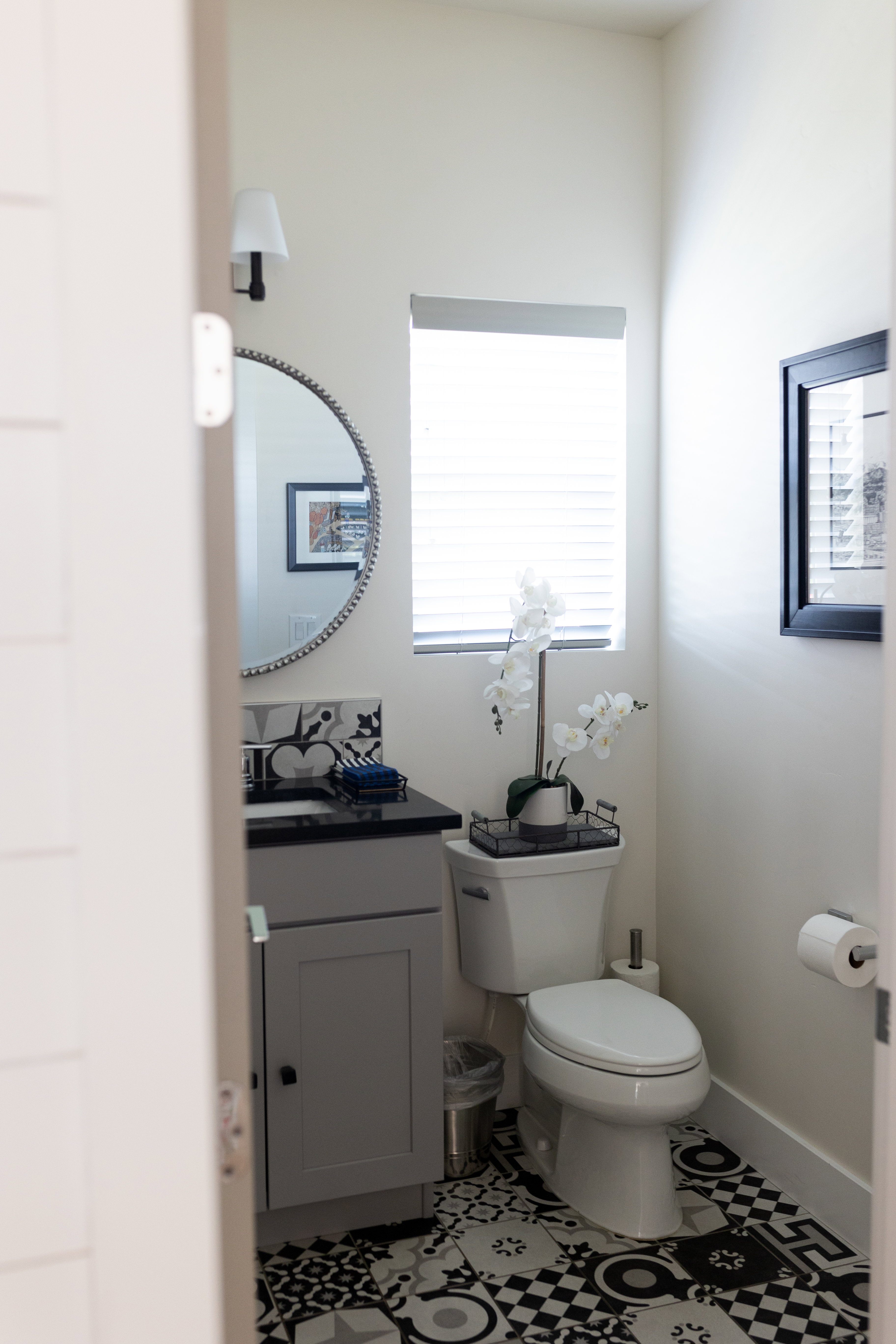 Main Floor powder room/half bath featuring a black and white patterned tile floor, a grey vanity with a dark countertop, and a round wall mirror