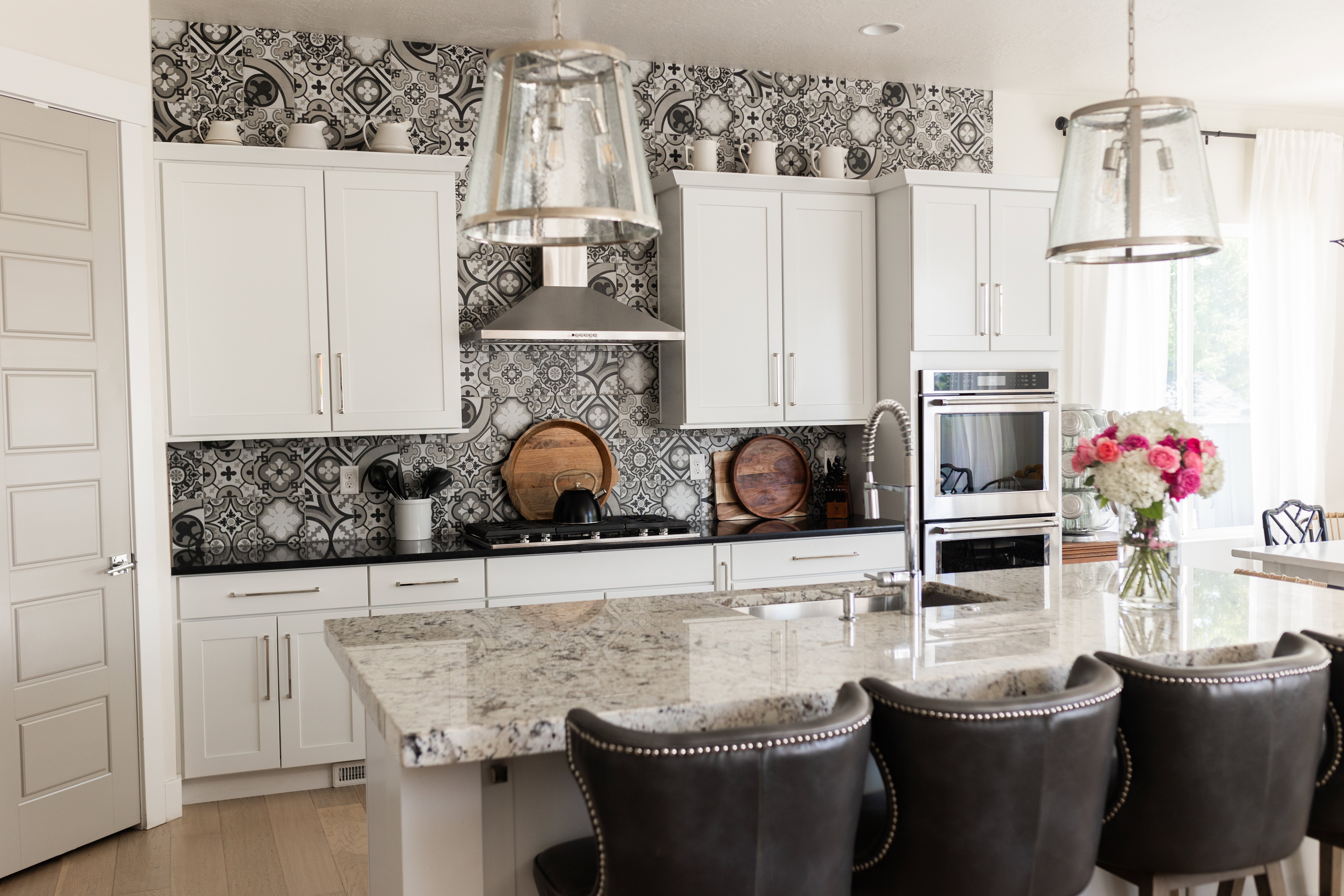 Kitchen featuring a patterned tile backsplash, stainless steel appliances, white cabinetry, a large kitchen island with a stone countertop, and pendant lighting fixtures