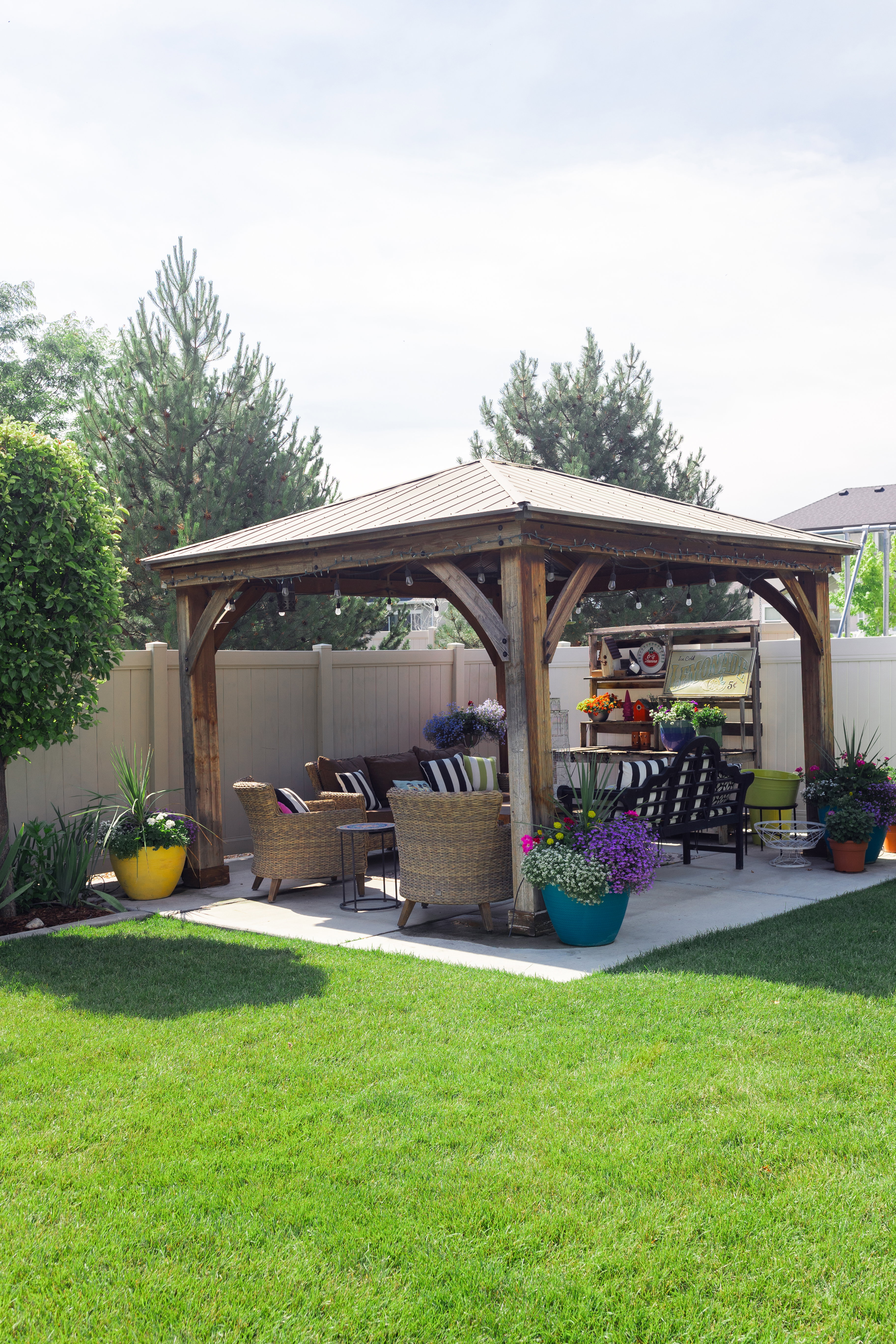 Backyard featuring a wood-frame gazebo with a metal roof, a concrete patio, a manicured lawn, and perimeter fencing.