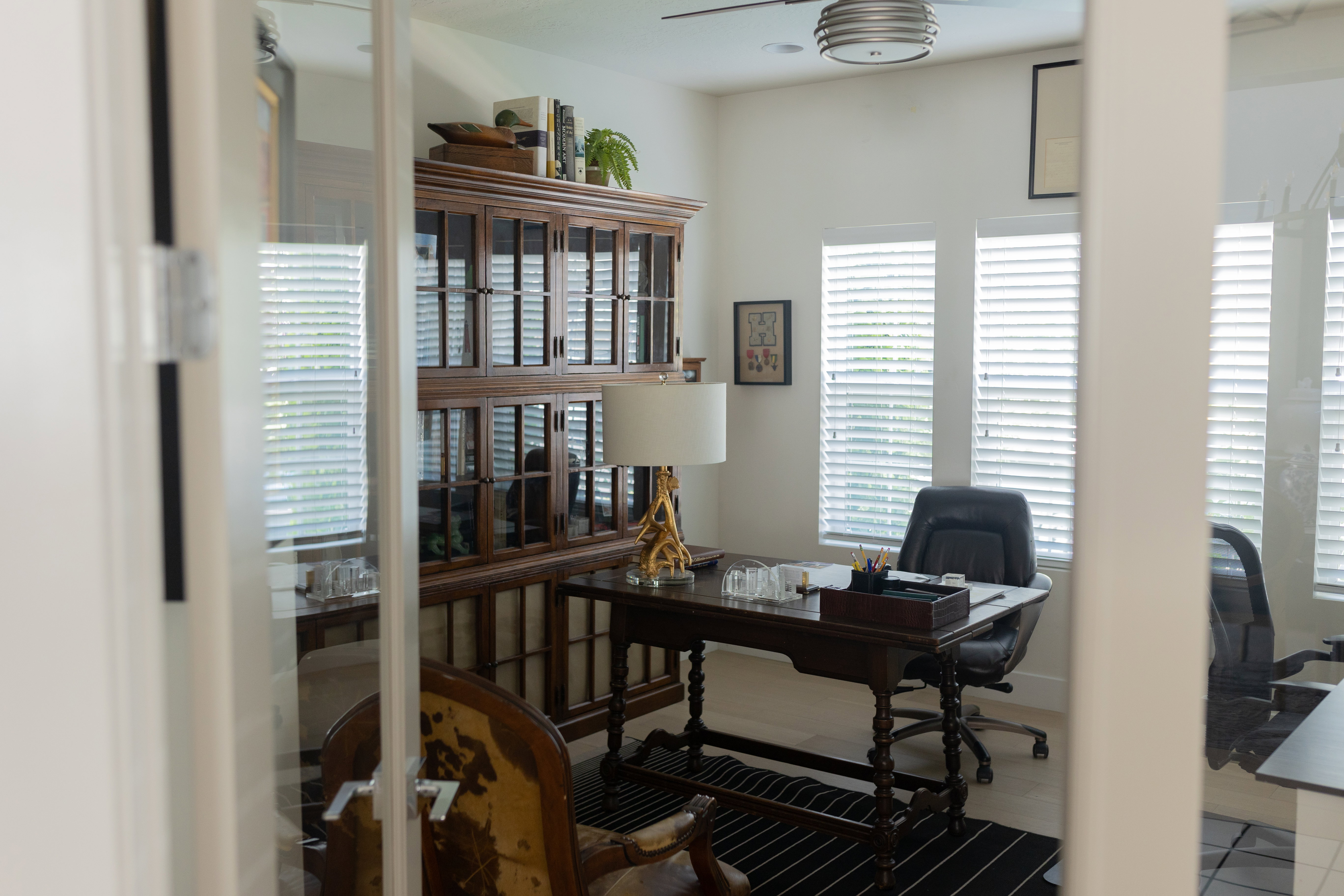 Office space featuring glass French doors, multiple windows with blinds, a ceiling fan, and light-toned flooring