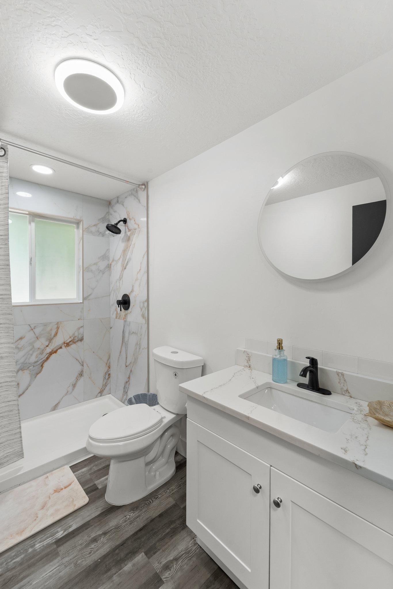 Bathroom featuring a walk-in shower with marble-look tile surround and matte black fixtures