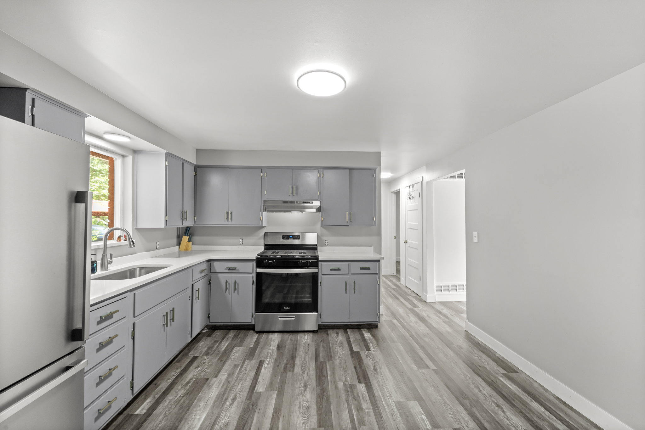 Modern kitchen featuring gray cabinetry, stainless steel appliances, light countertops, a stainless steel sink with a gooseneck faucet, and wood-finish flooring