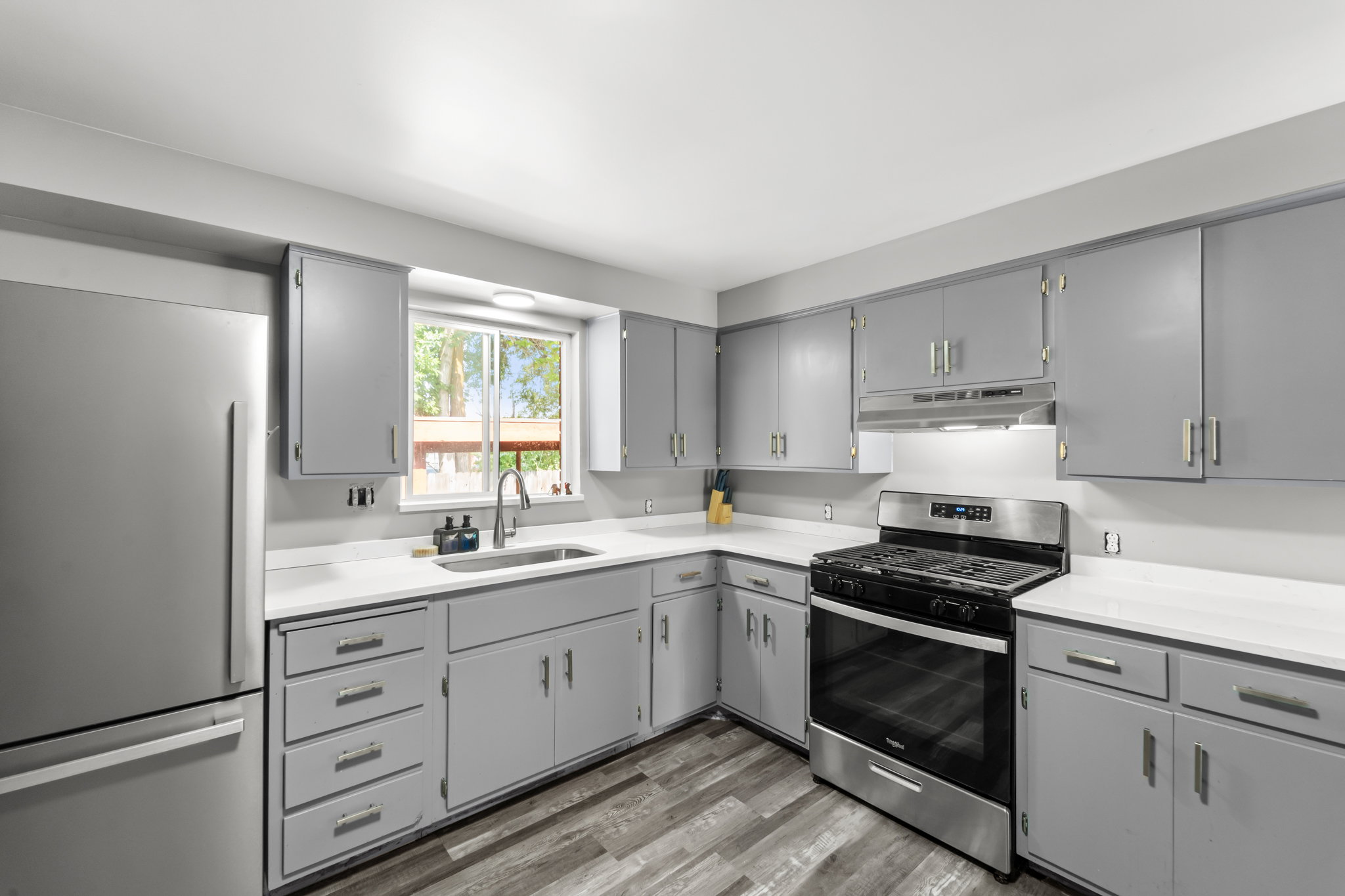 Kitchen featuring gray cabinetry, white countertops, stainless steel appliances, and wood-finish flooring