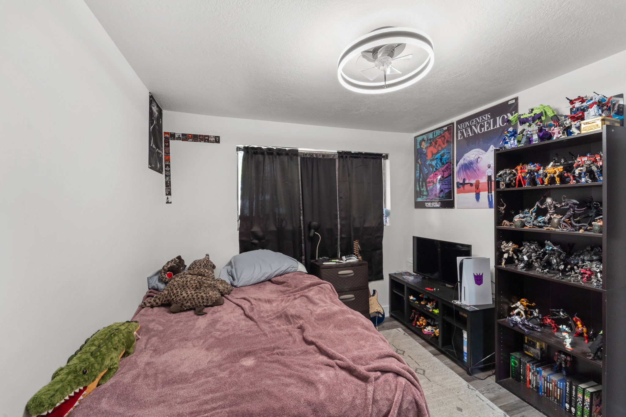 Bedroom featuring a ceiling fan with integrated lighting, window with dark drapes, and light-colored walls