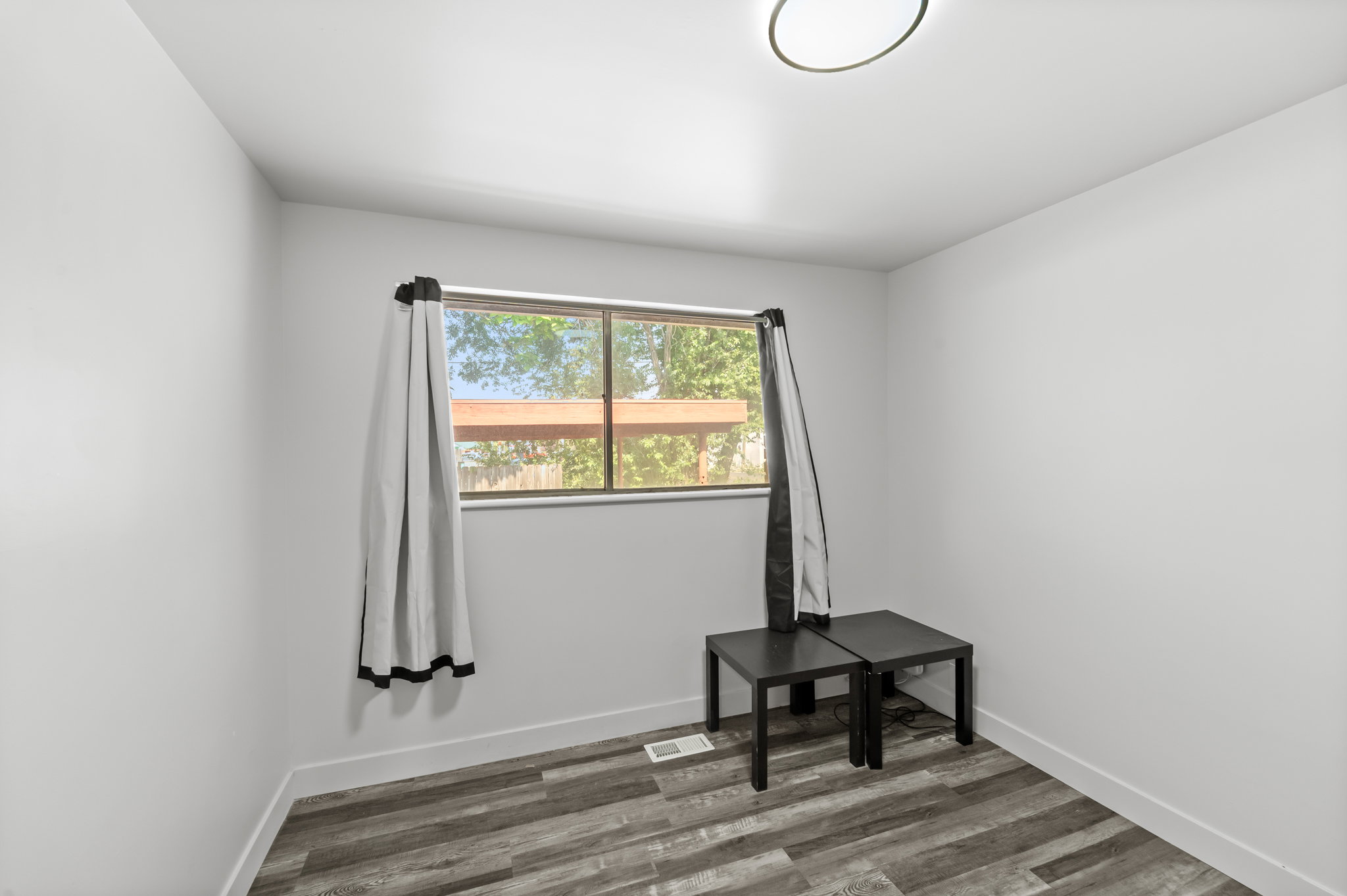 Room featuring wood-look flooring, a window with exterior views, white baseboards, and a flush-mount ceiling light