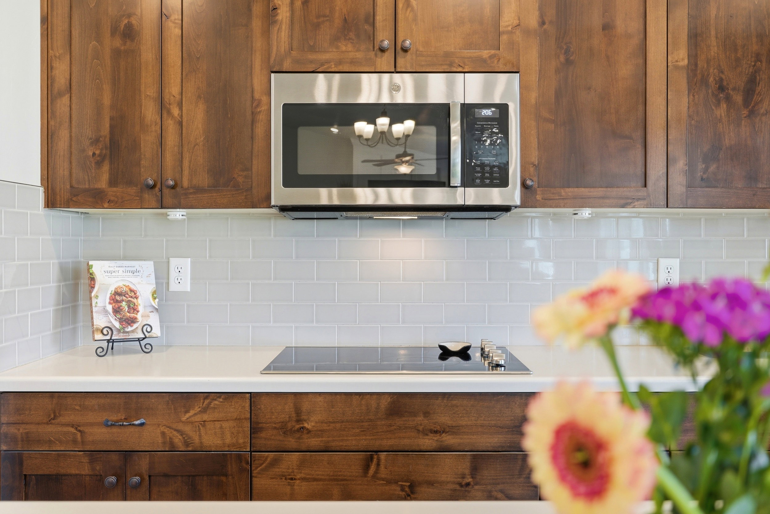 Kitchen featuring wood cabinetry, light-toned countertops, a stainless steel microwave, a black induction cooktop, and subway tile backsplash