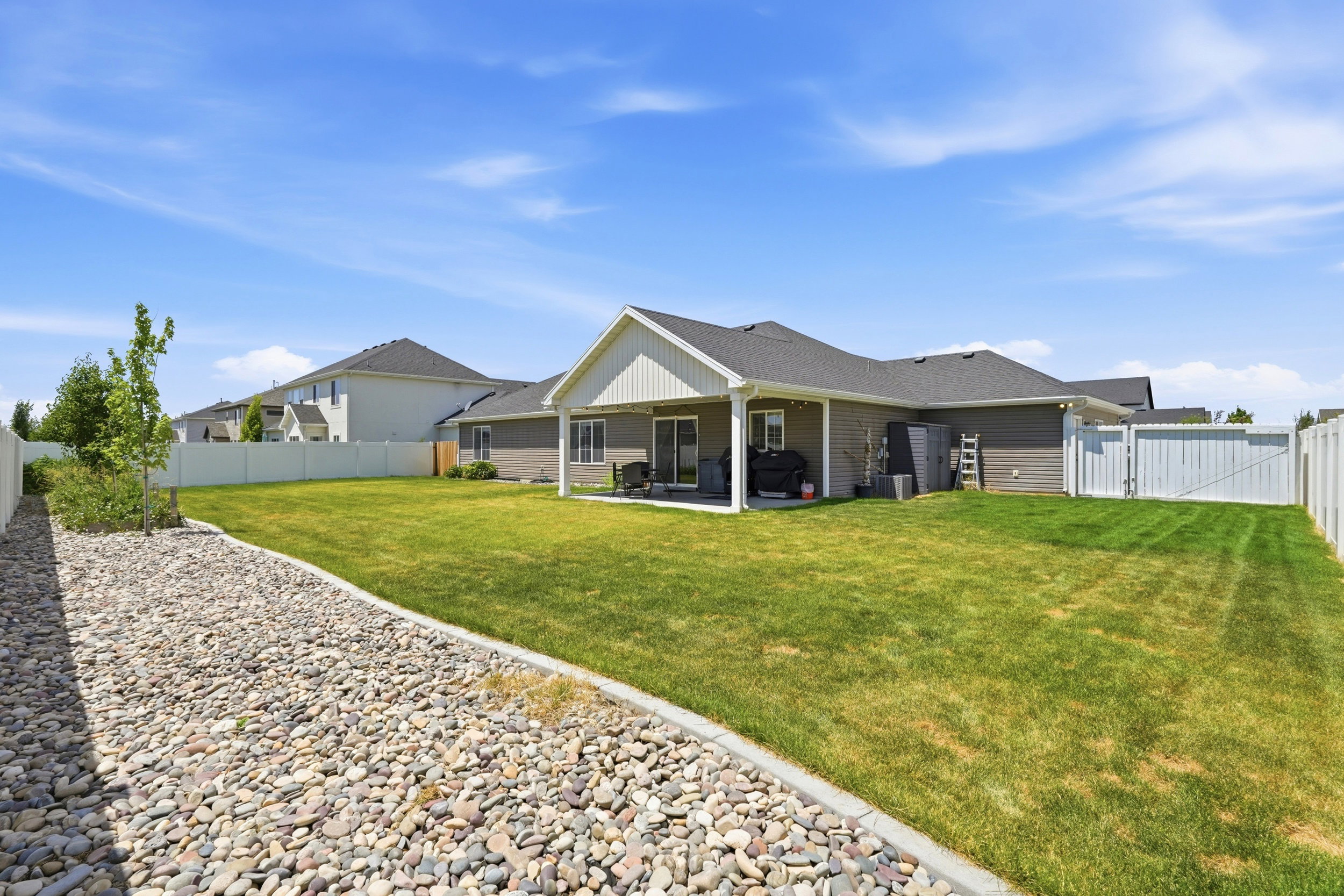 Expansive backyard featuring a manicured lawn, a covered patio, and a decorative rock bed