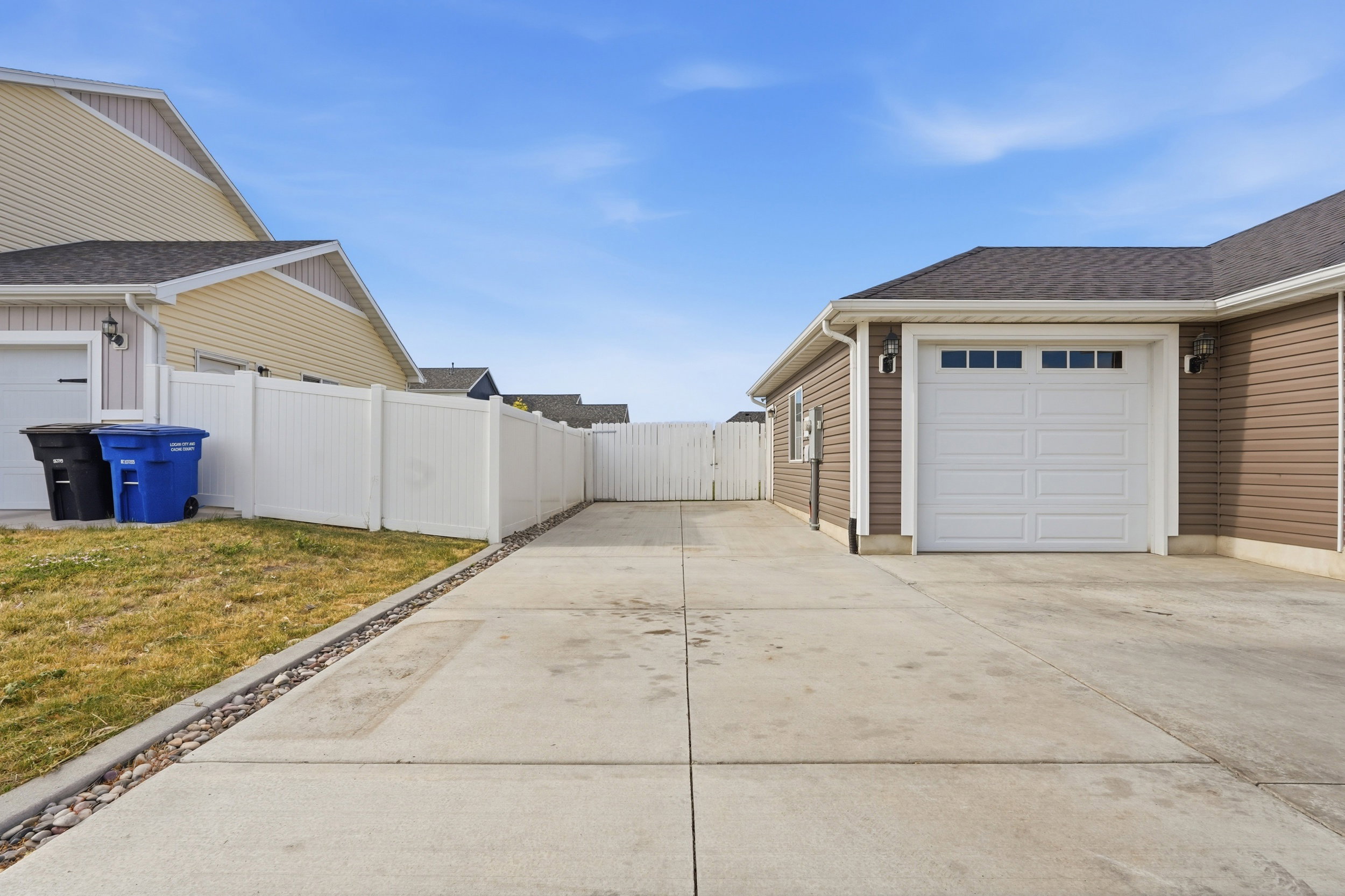 Concrete driveway extending along the property, bordered by a white vinyl fence