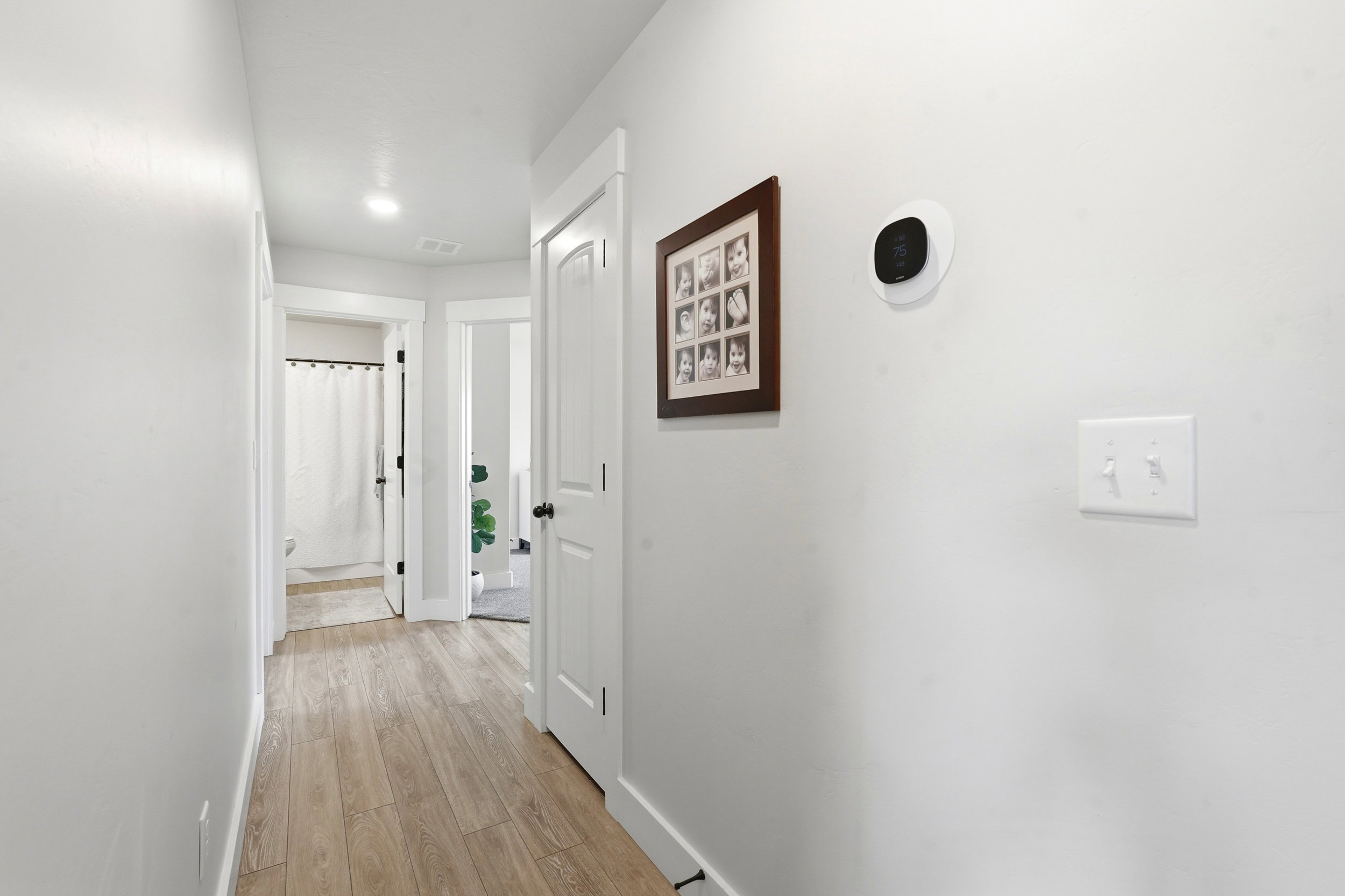 Hallway featuring wood-finish flooring, recessed lighting, white walls, and a modern thermostat