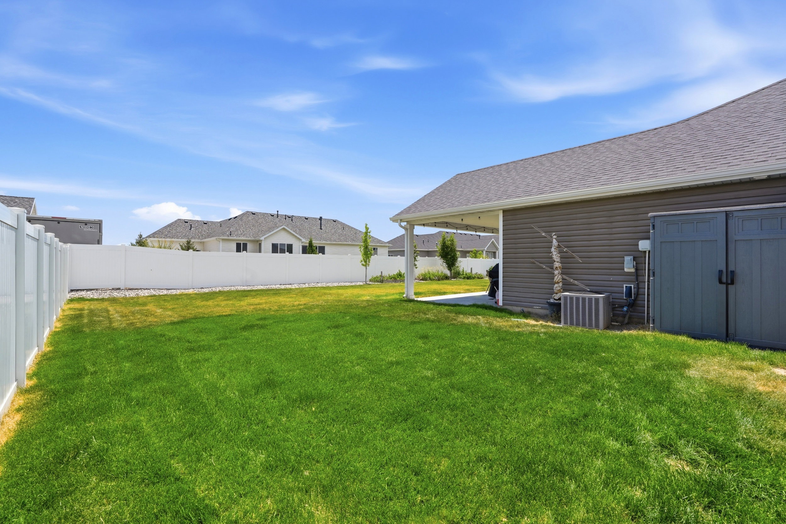 Spacious grassy yard featuring a white privacy fence and a covered concrete patio