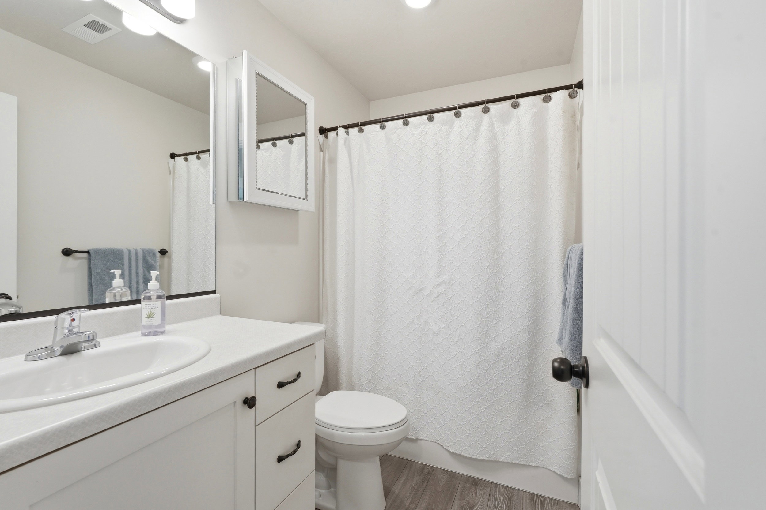 Bathroom featuring a white vanity with integrated sink, a large wall-mounted mirror, recessed lighting, and wood-finish flooring