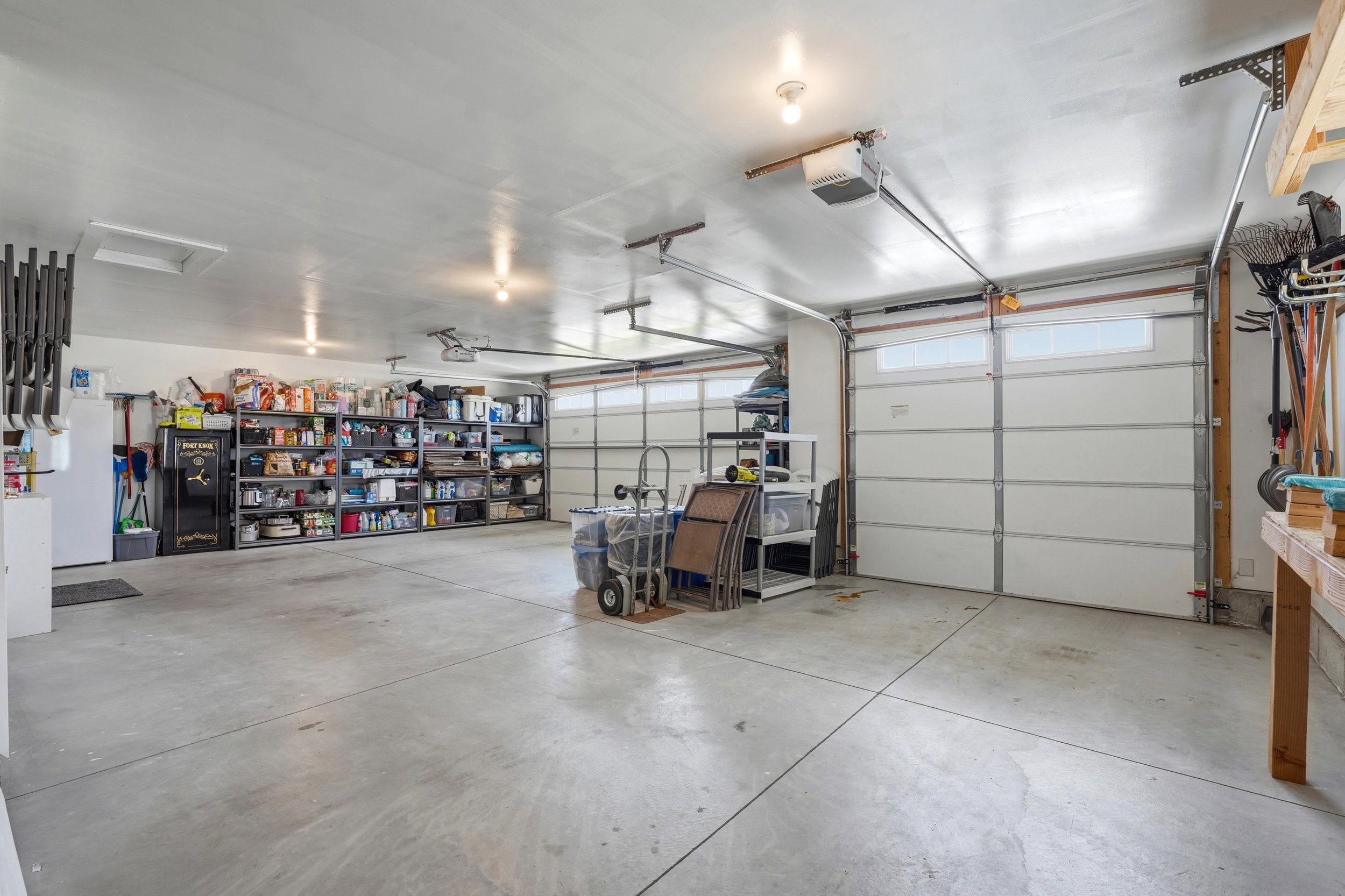 Spacious garage featuring a concrete floor, two white panel garage doors with upper windows, and overhead lighting