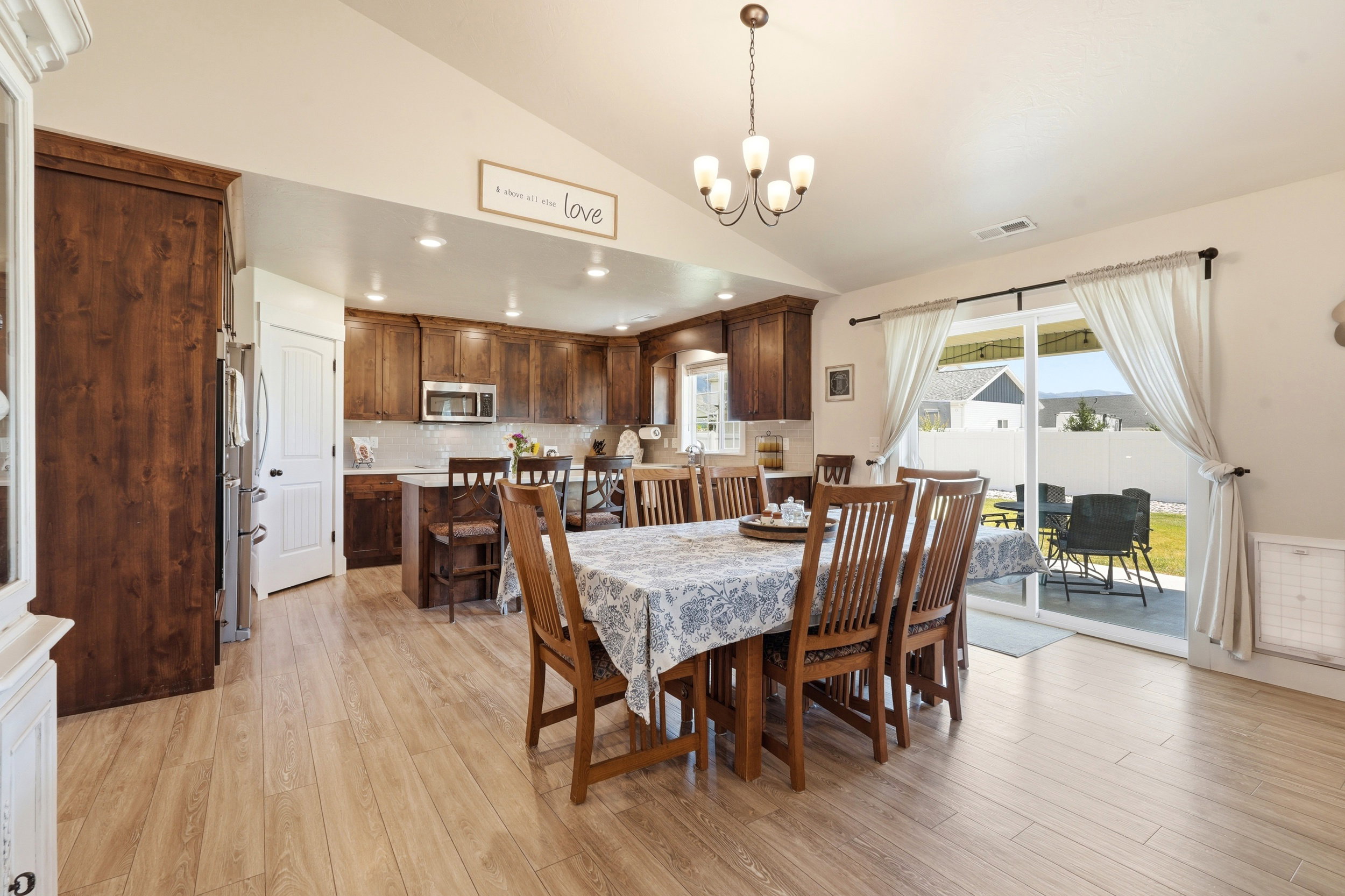 Open concept kitchen and dining area featuring wood-finish flooring, vaulted ceilings, dark wood cabinetry, and a sliding glass door to the exterior patio