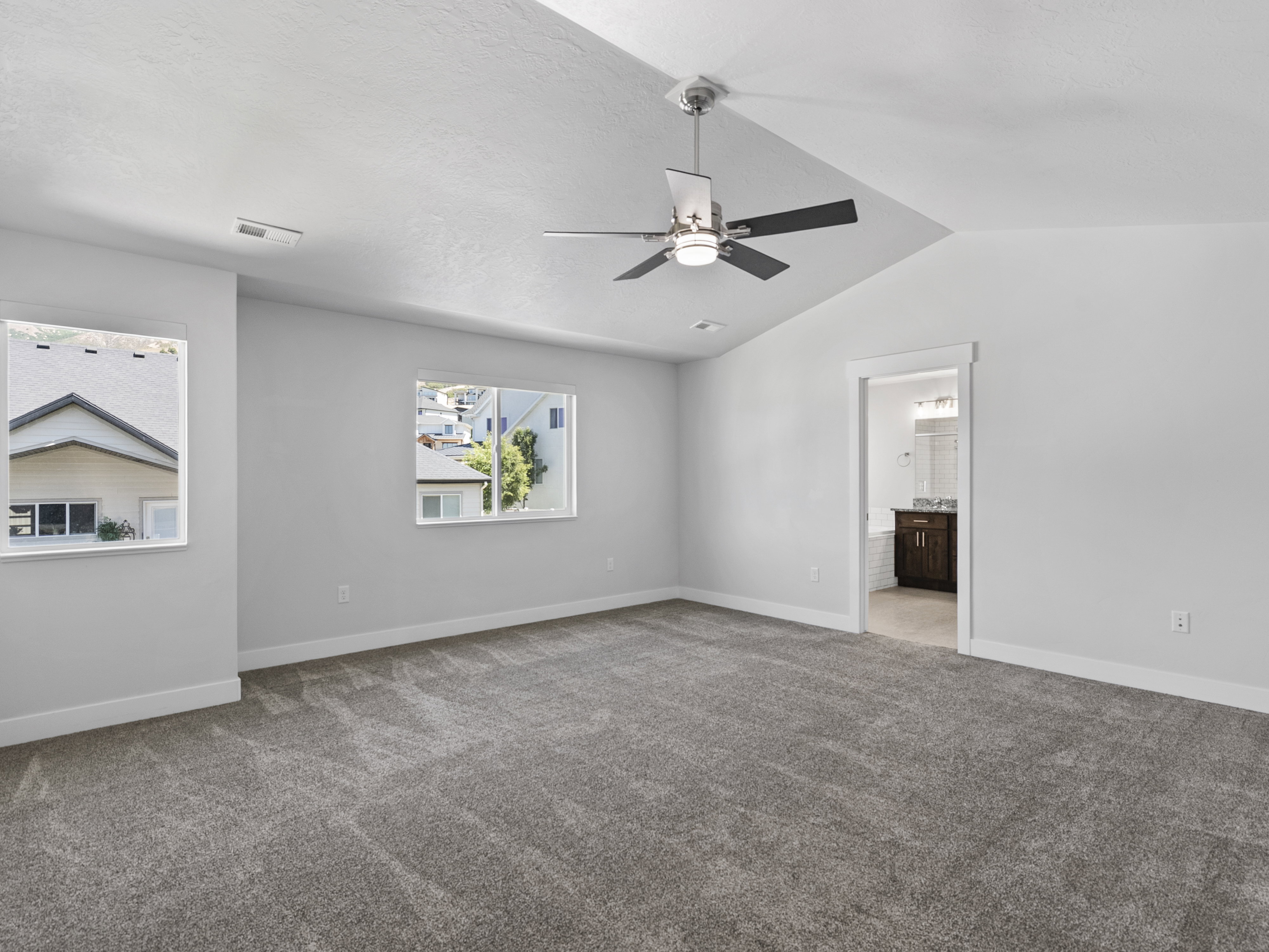 Spacious room featuring vaulted ceilings, a ceiling fan with integrated lighting, and two windows