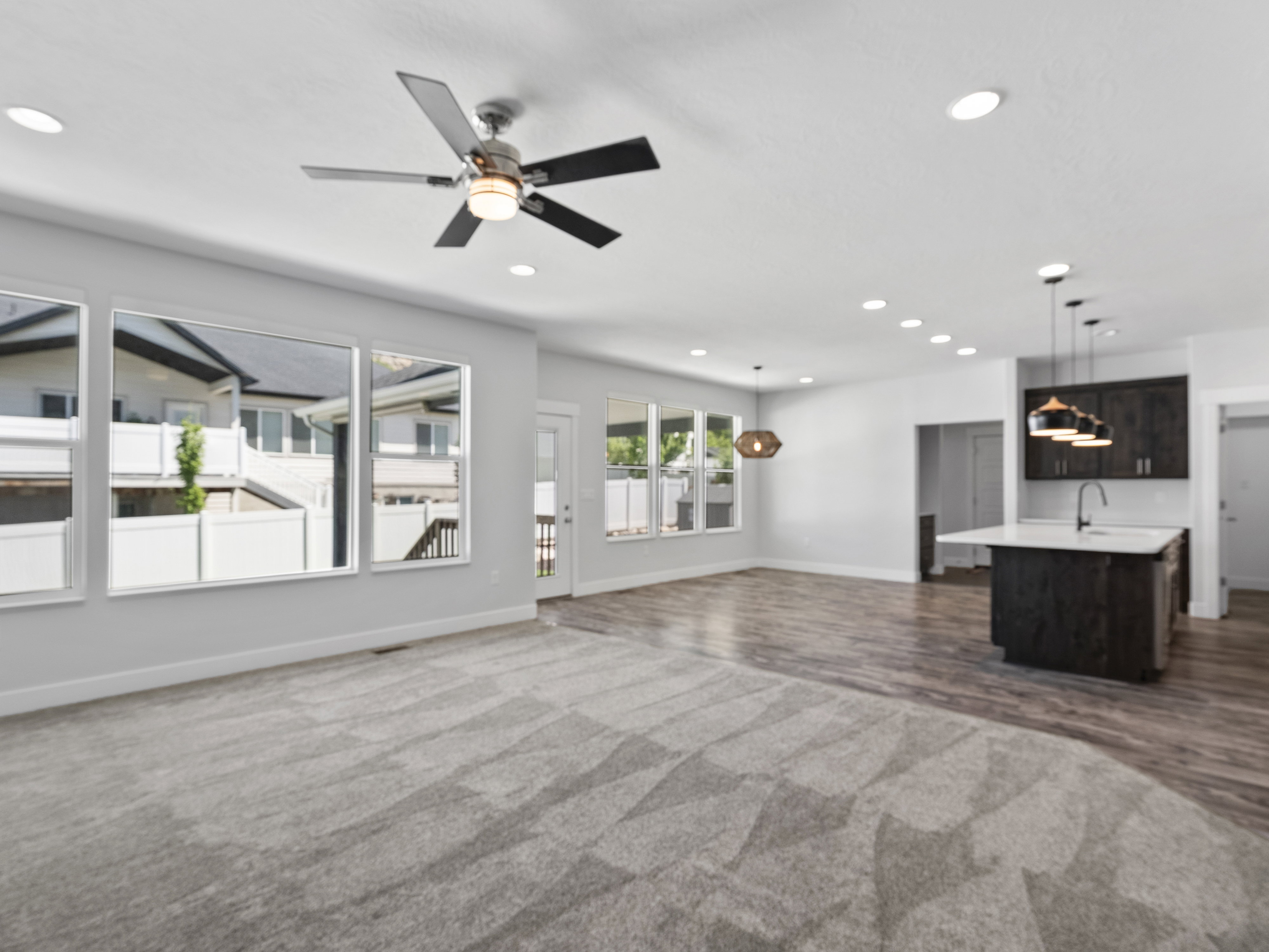 Open-concept living space featuring a gray patterned carpet, wood-finish flooring, a kitchen island with pendant lighting, and multiple windows