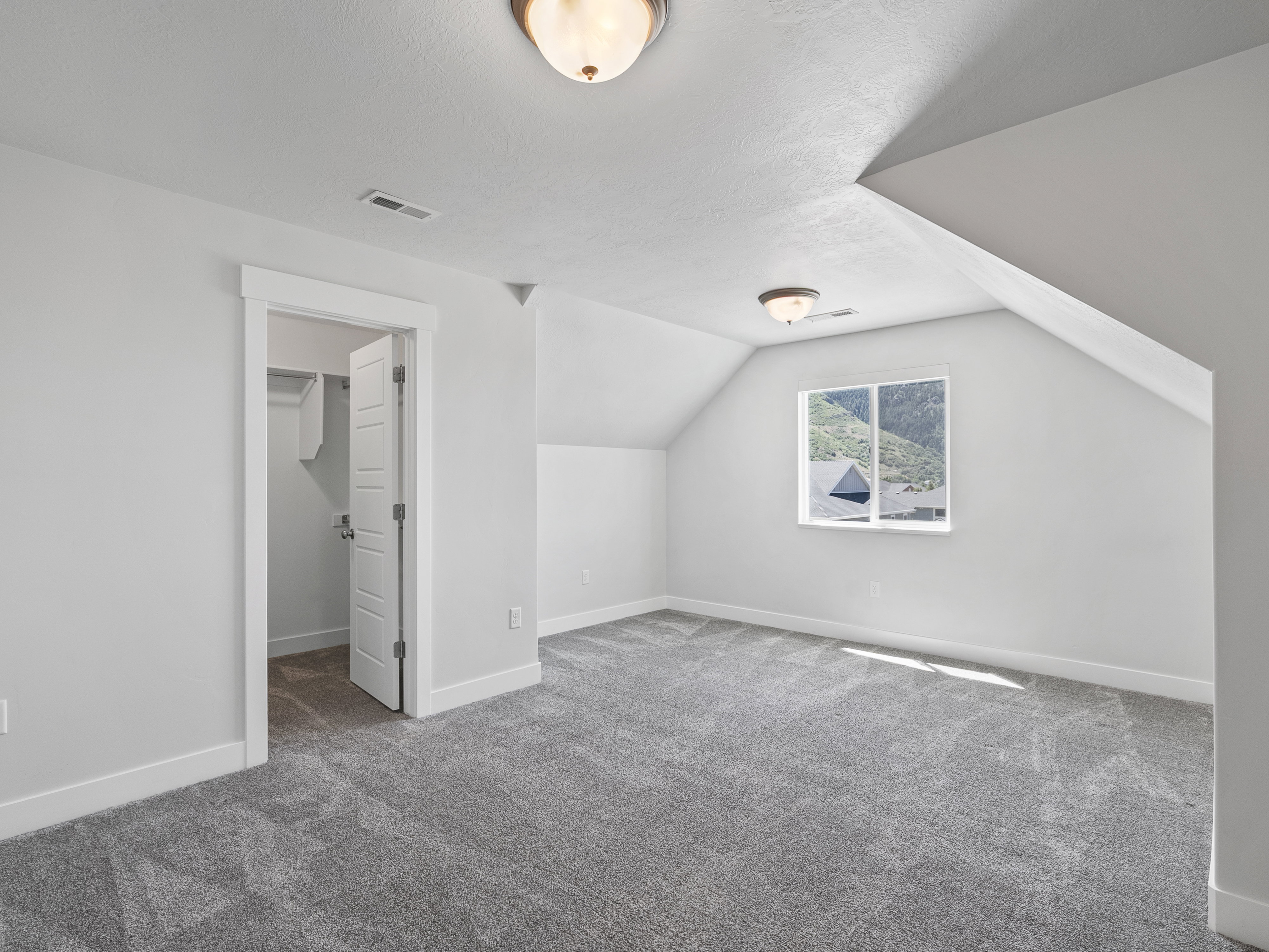 Carpeted room featuring a white interior door, a single window, and sloped ceiling details
