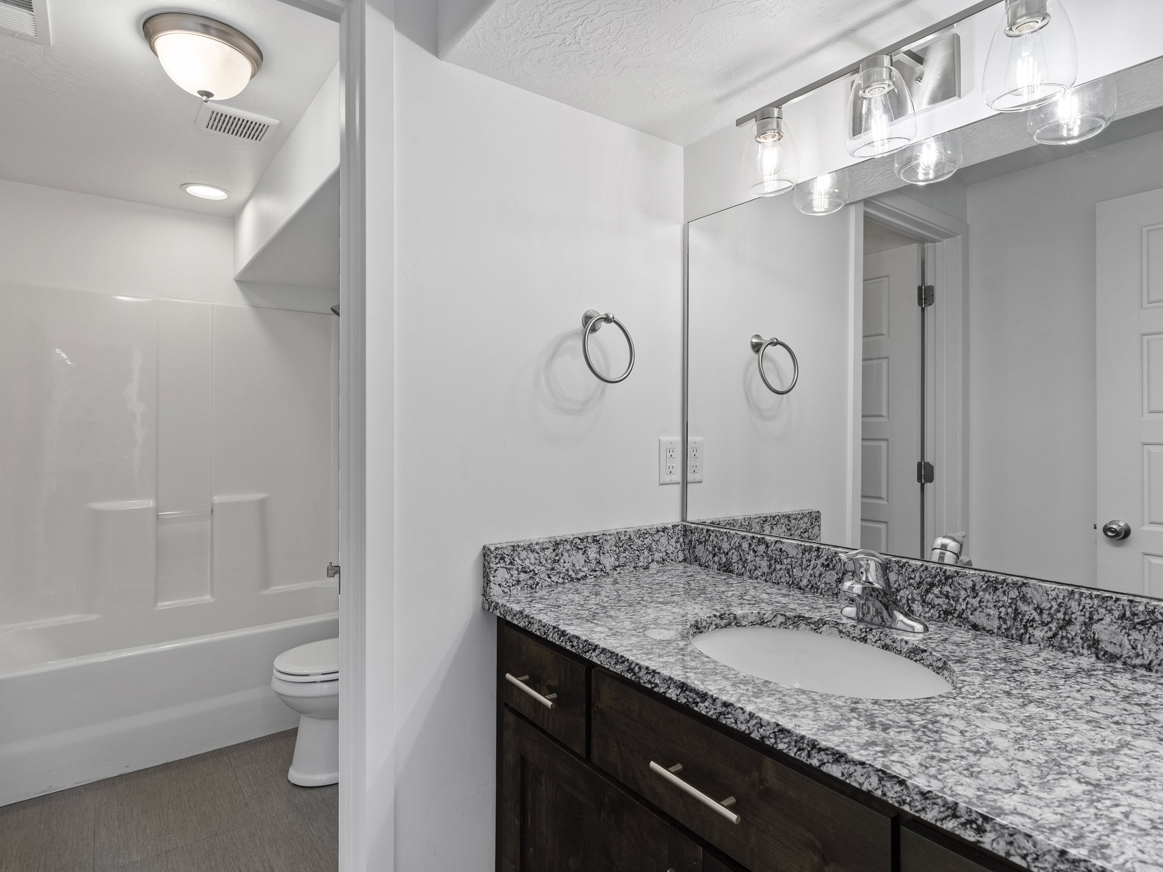 Bathroom featuring a dark wood-finish vanity with a light speckled countertop, an integrated sink, and a large mirror