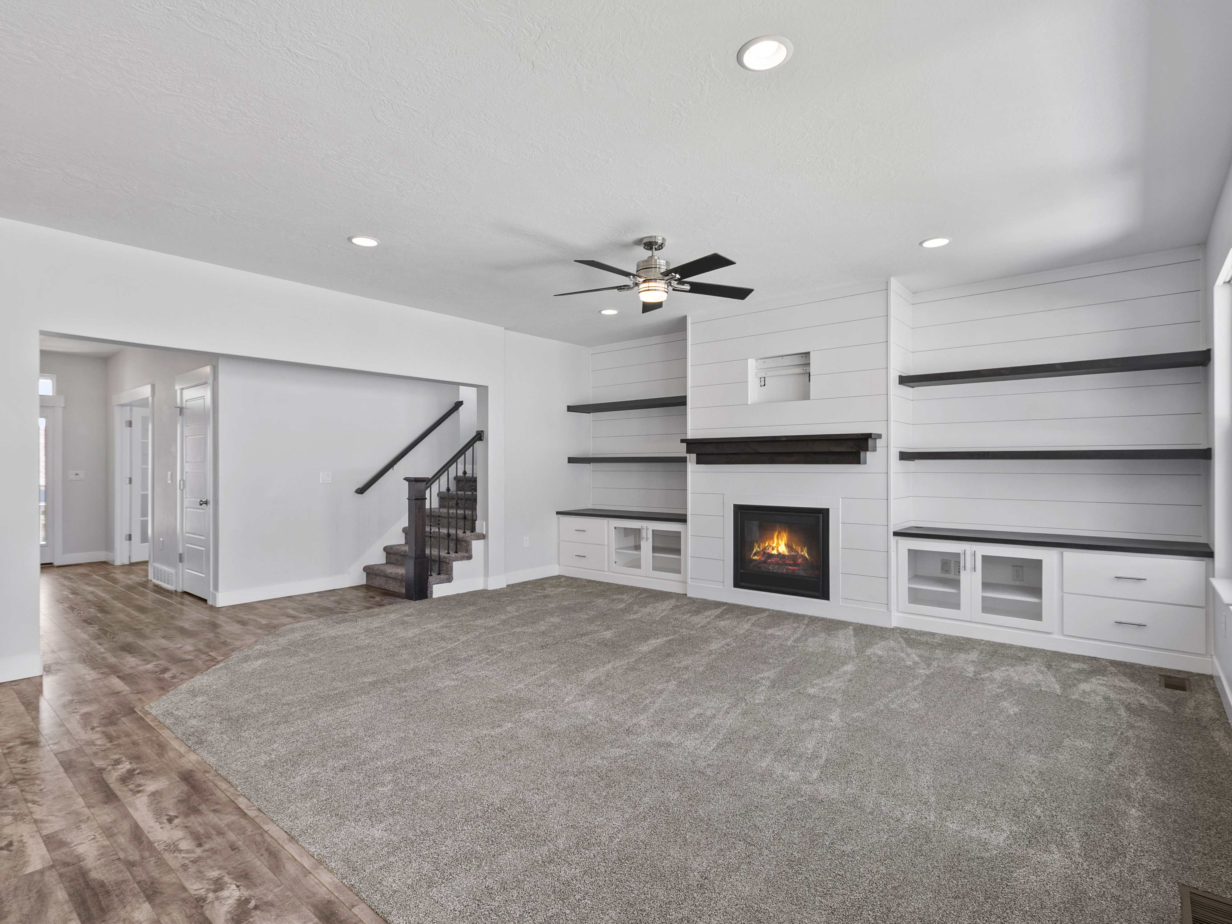 Carpeted living area featuring a fireplace with shiplap surround, built-in shelving and cabinetry, recessed lighting, and wood-finish flooring