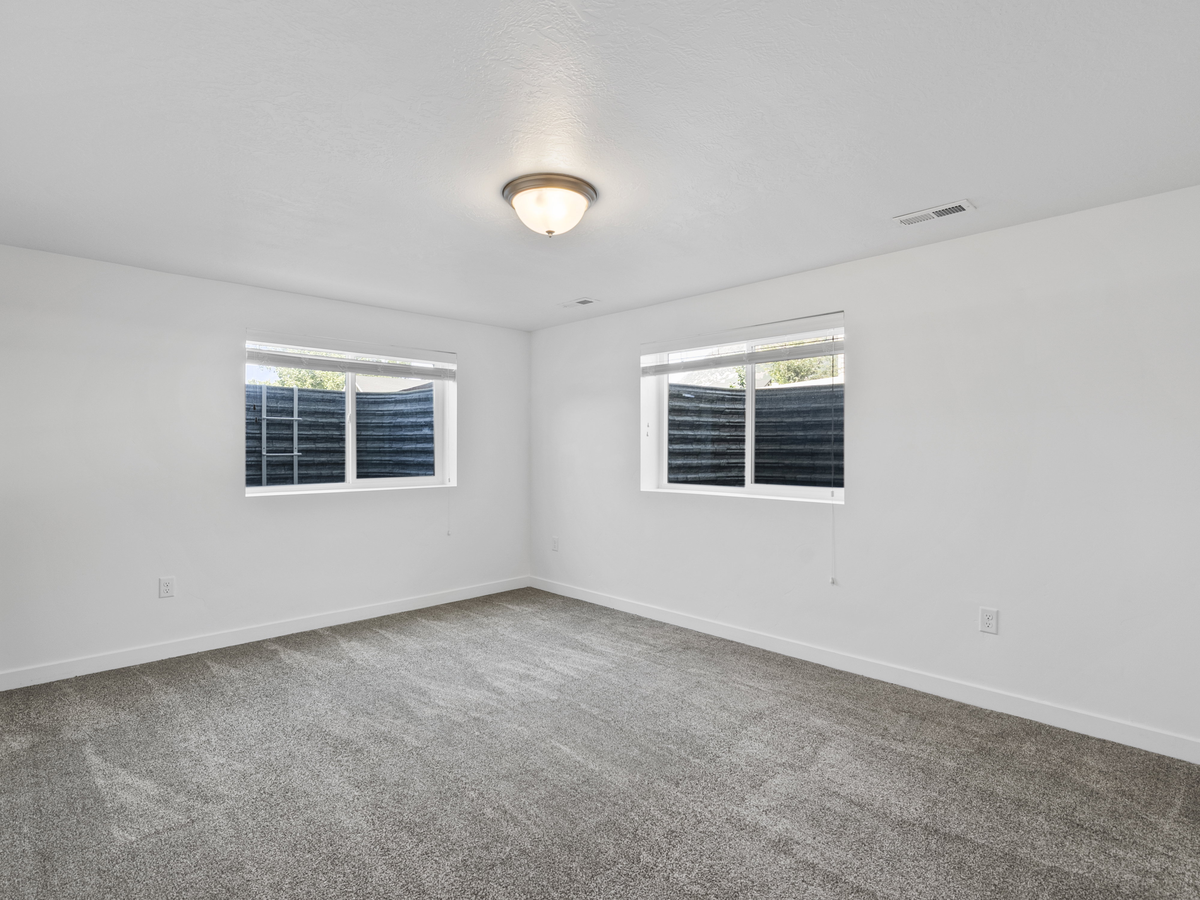 Carpeted room with white walls, two windows featuring horizontal blinds, and a flush-mount ceiling light fixture