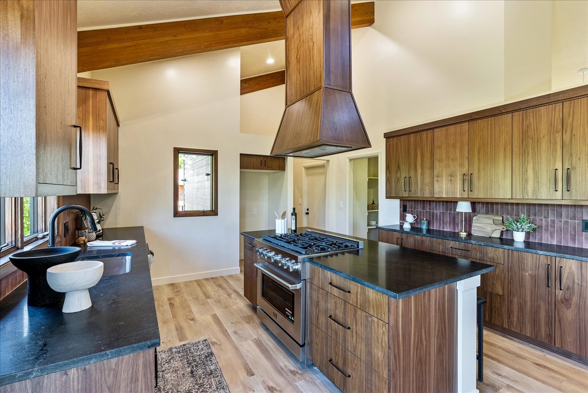 Kitchen featuring vaulted ceilings with exposed wood beams, wood-finish flooring, a central island with a gas range, dark countertops, and extensive wood cabinetry