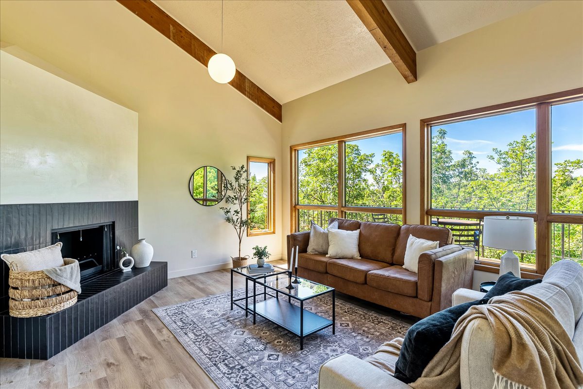Vaulted ceiling with exposed wood beams, wood-finish flooring, and a modern fireplace with a dark tile surround