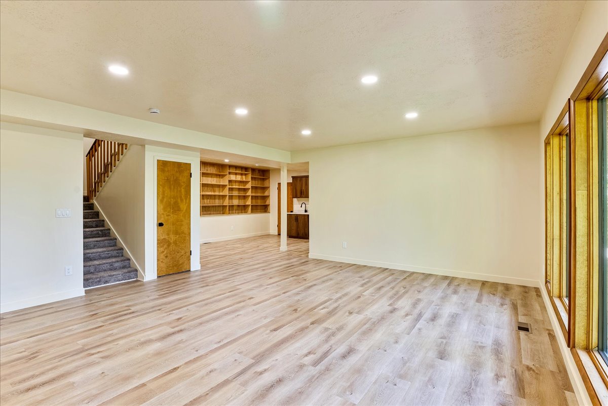 Spacious open-concept room featuring light wood-finish flooring, recessed lighting, and a prominent window bank with natural wood trim