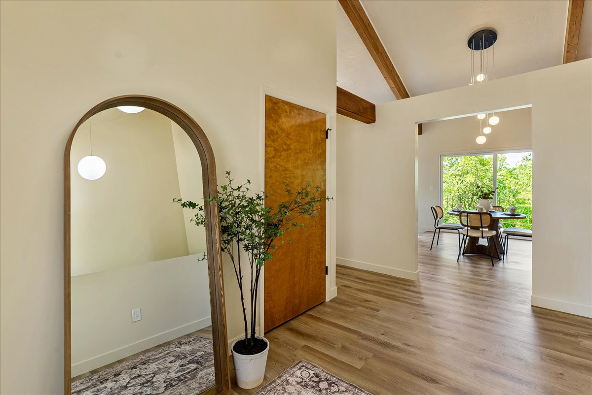 Bright interior space featuring wood-finish flooring, exposed ceiling beams, and a natural wood door