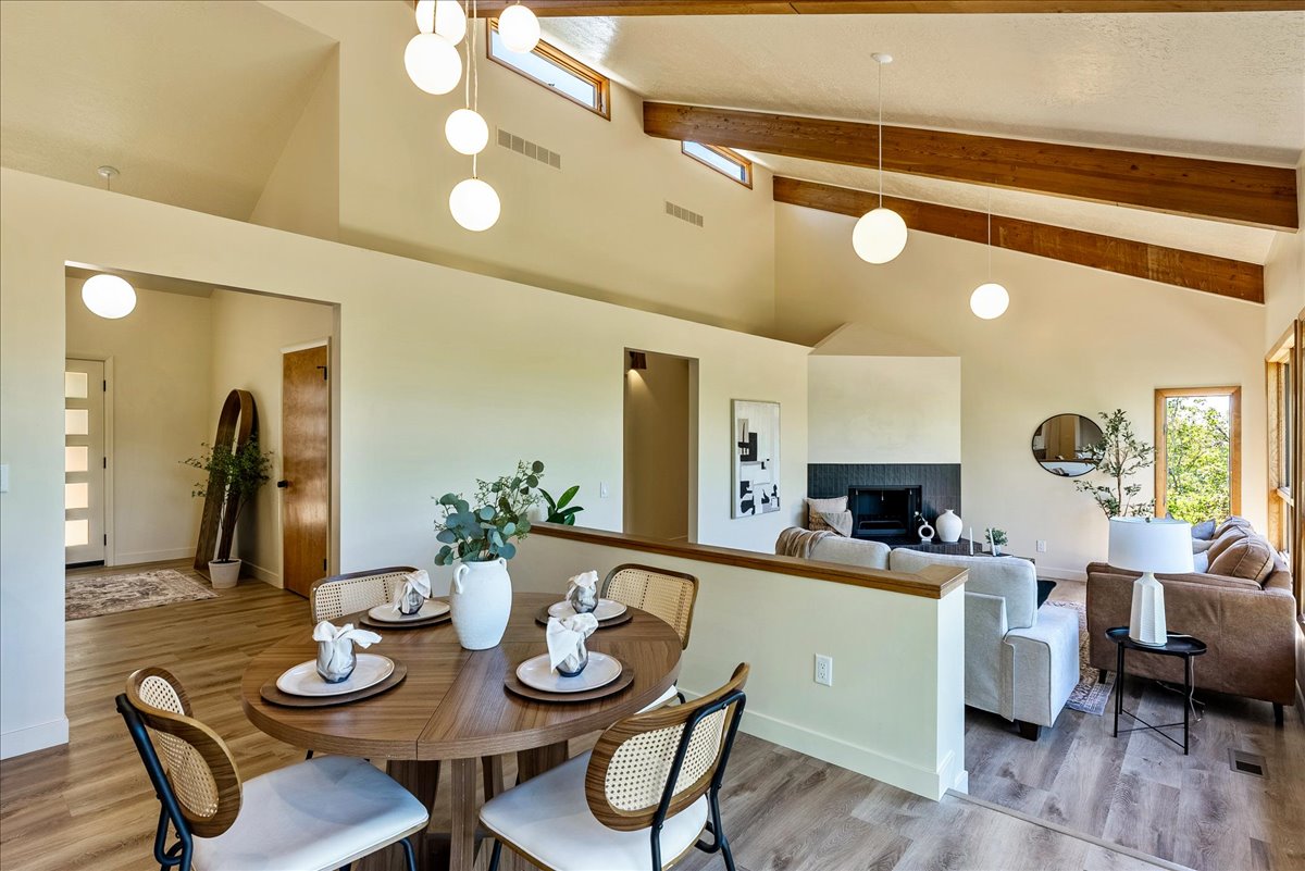 Open-concept living area with vaulted ceilings featuring exposed wood beams and abundant natural light from upper transom windows