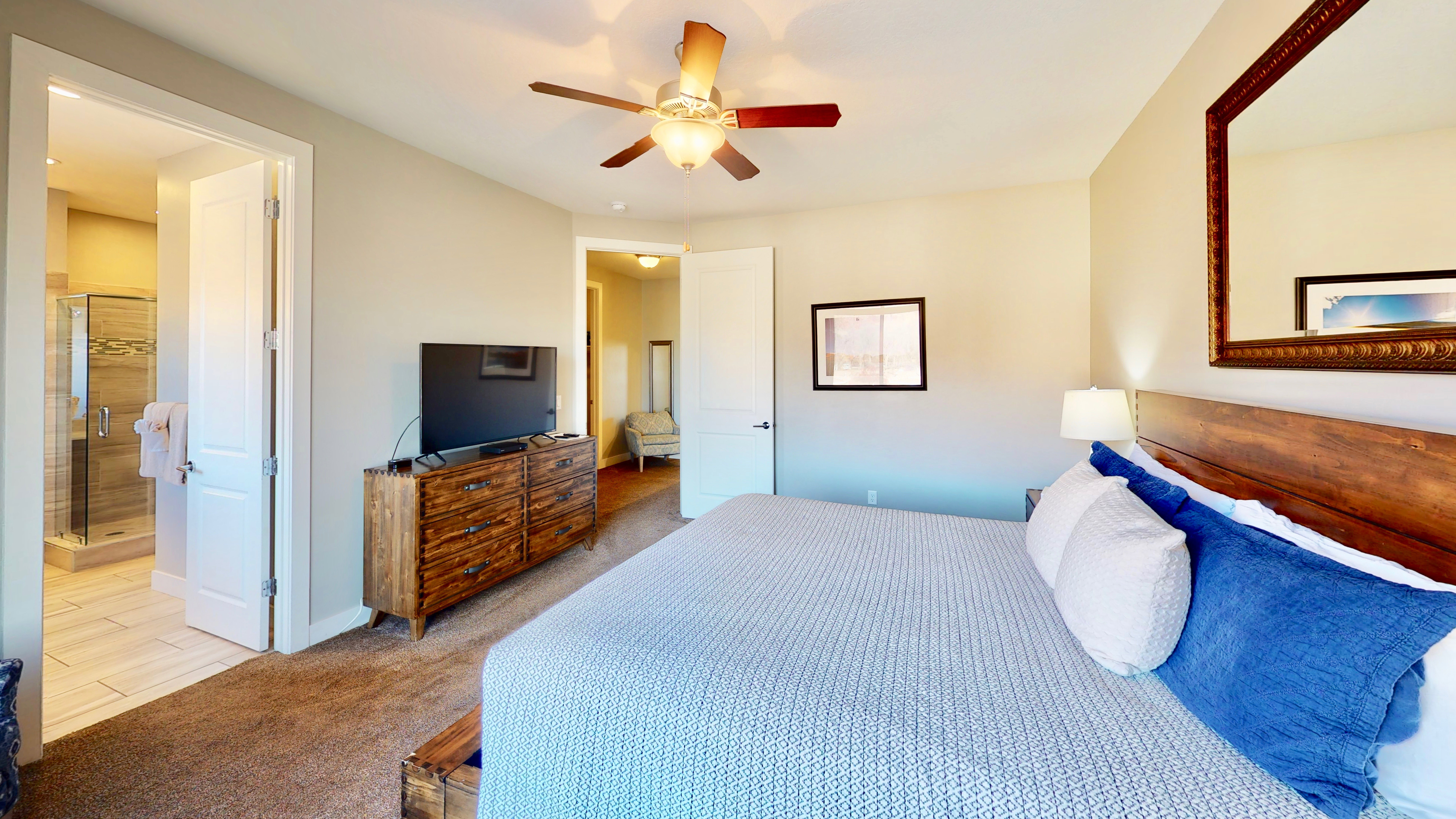 Bedroom featuring a ceiling fan with light fixture, wood-finish headboard, and an en-suite bathroom with a glass-enclosed shower and tiled flooring