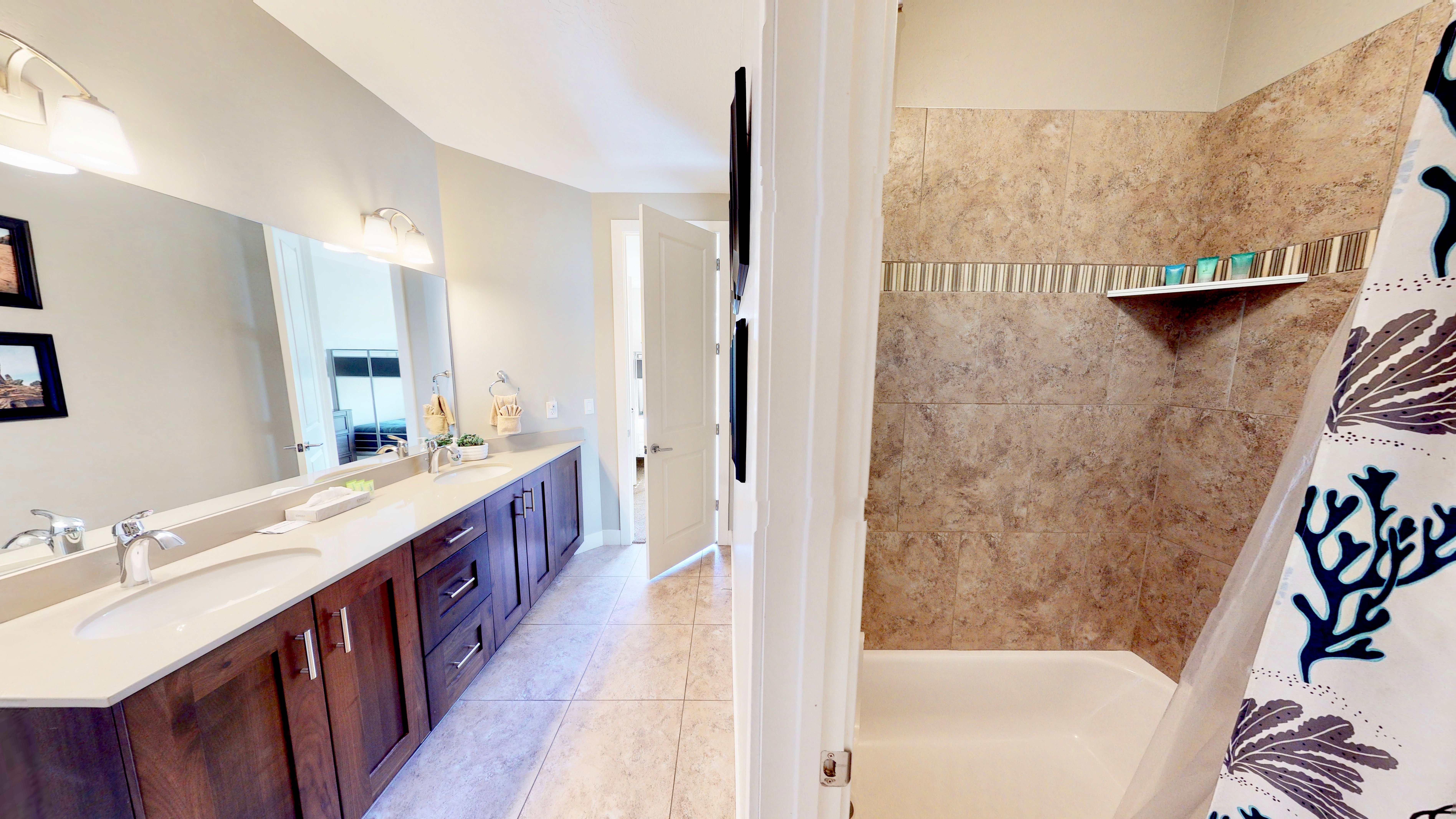 Bathroom featuring a dual vanity with undermount sinks and dark wood cabinetry, a large wall-mounted mirror, and tile flooring