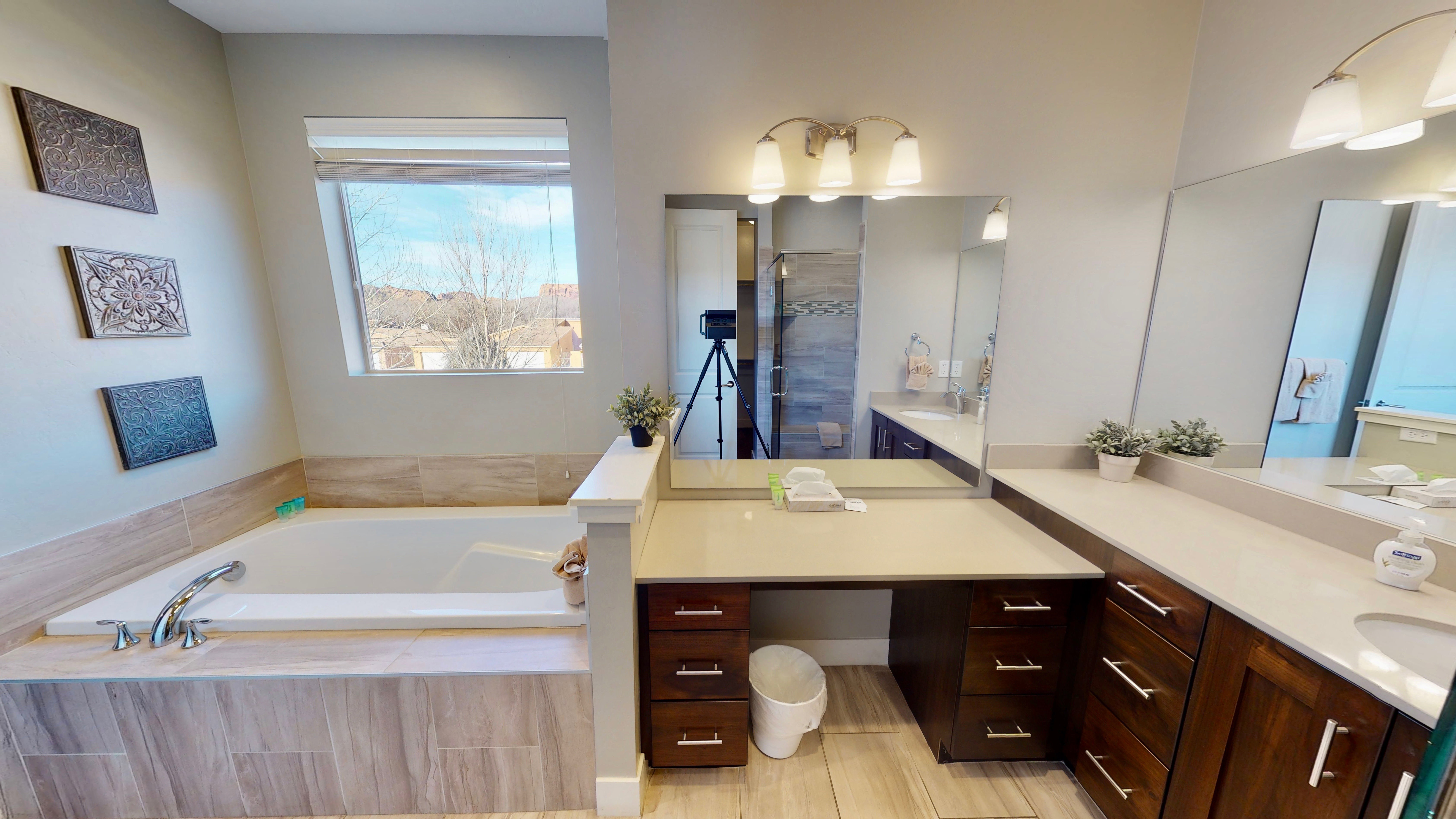 Spacious bath featuring an undermount tub with tiled surround, a large vanity with stone countertops, a dedicated makeup vanity, and multiple built-in storage drawers
