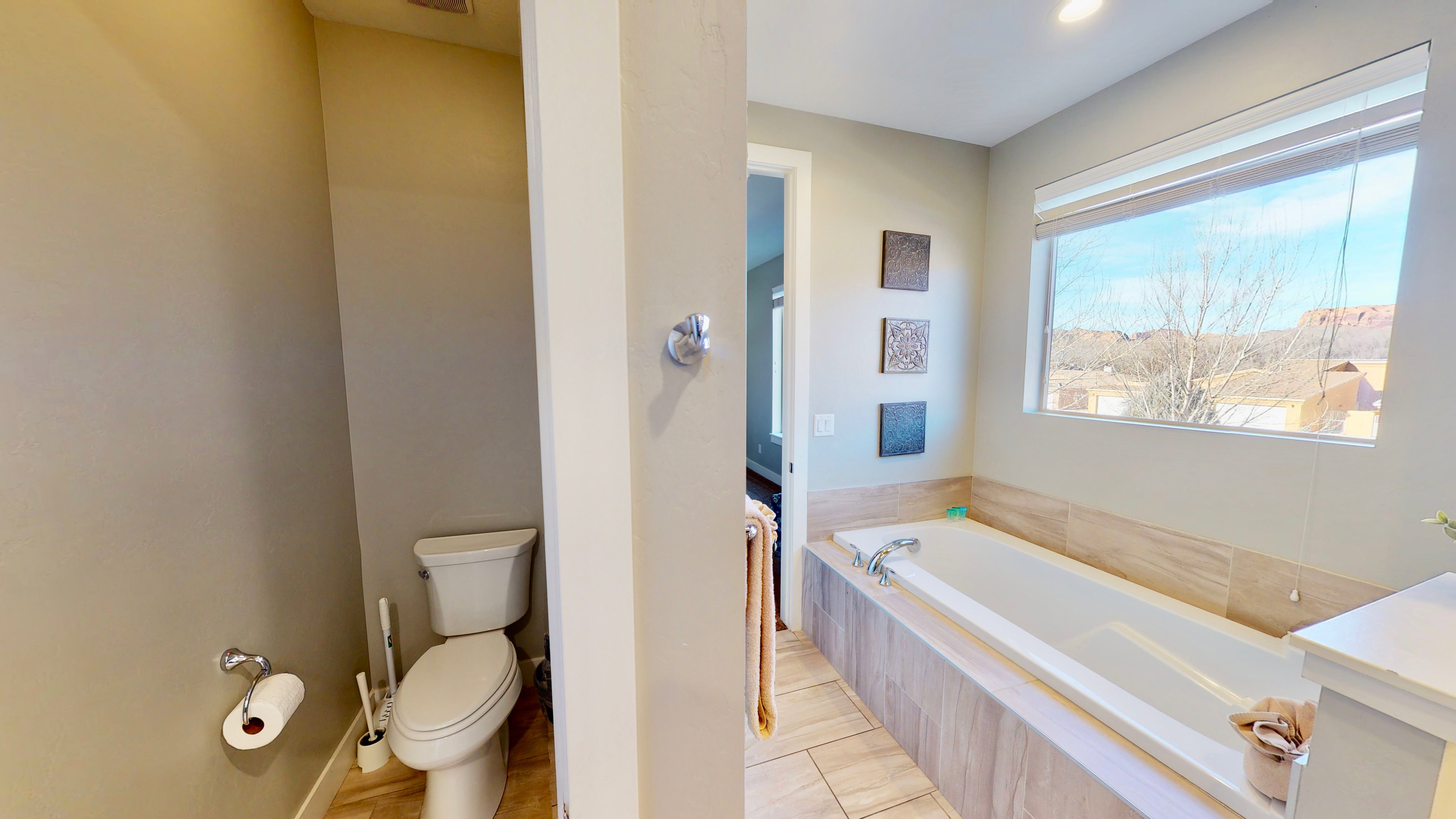 Soaking tub with a tiled surround, large window with outdoor scenery, and recessed lighting