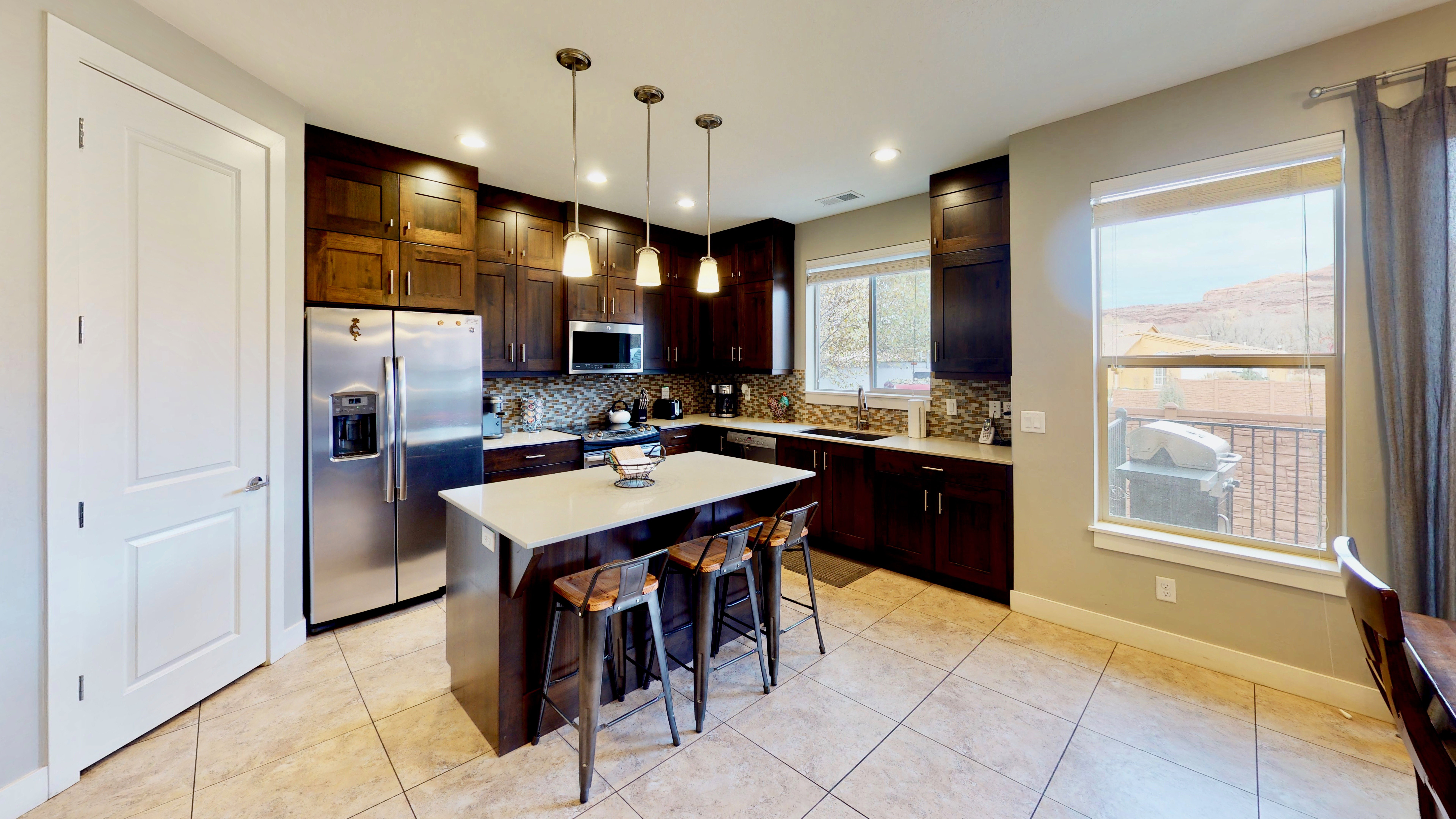 Contemporary kitchen featuring an island with seating, dark wood-finish cabinetry, stainless steel appliances, and a tiled backsplash