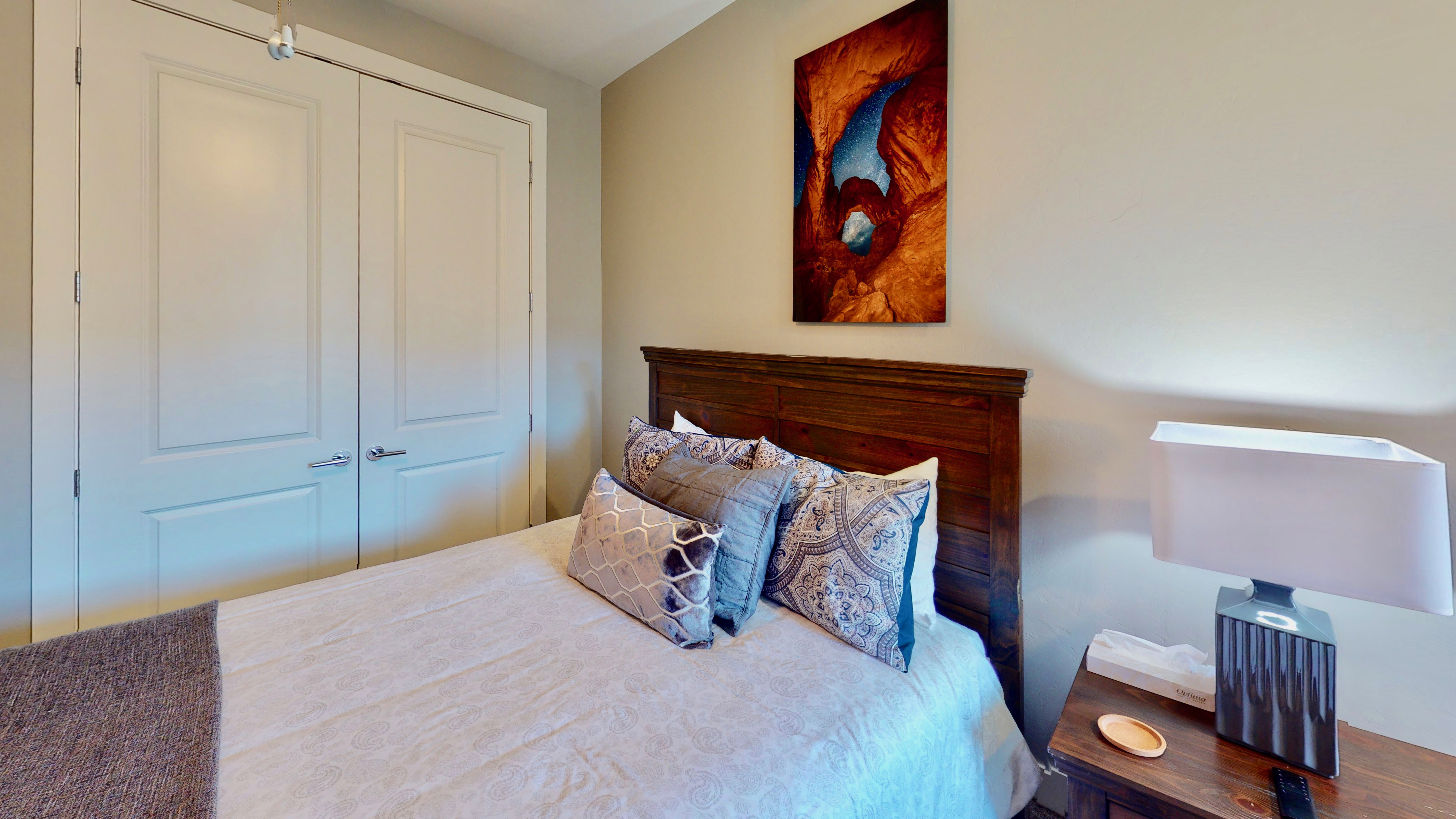 Bedroom featuring a paneled wood headboard, neutral wall paint, and double white closet doors with brushed nickel hardware