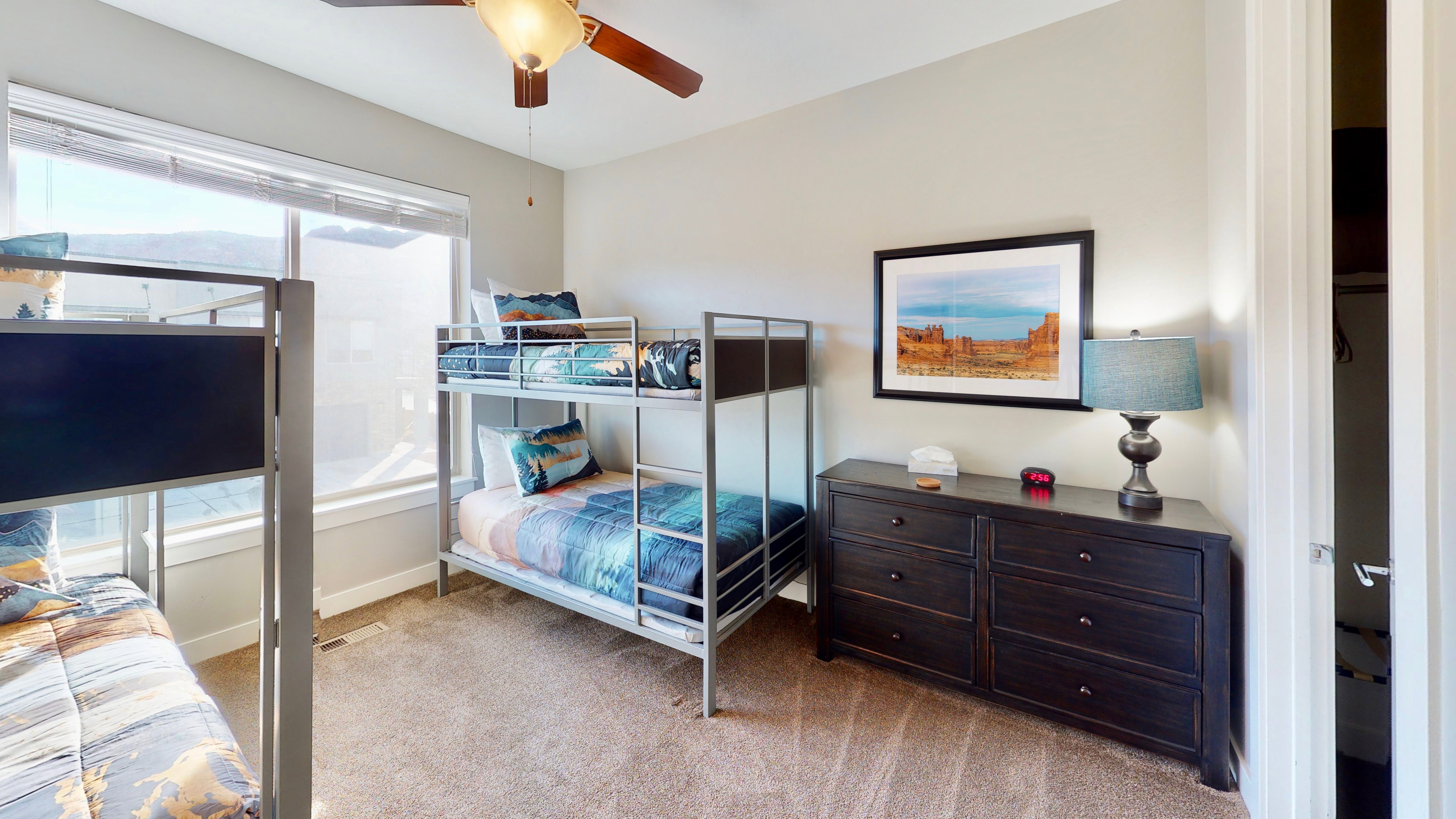 Carpeted room featuring a large window, a ceiling fan with integrated lighting, and a dark wood-finish dresser