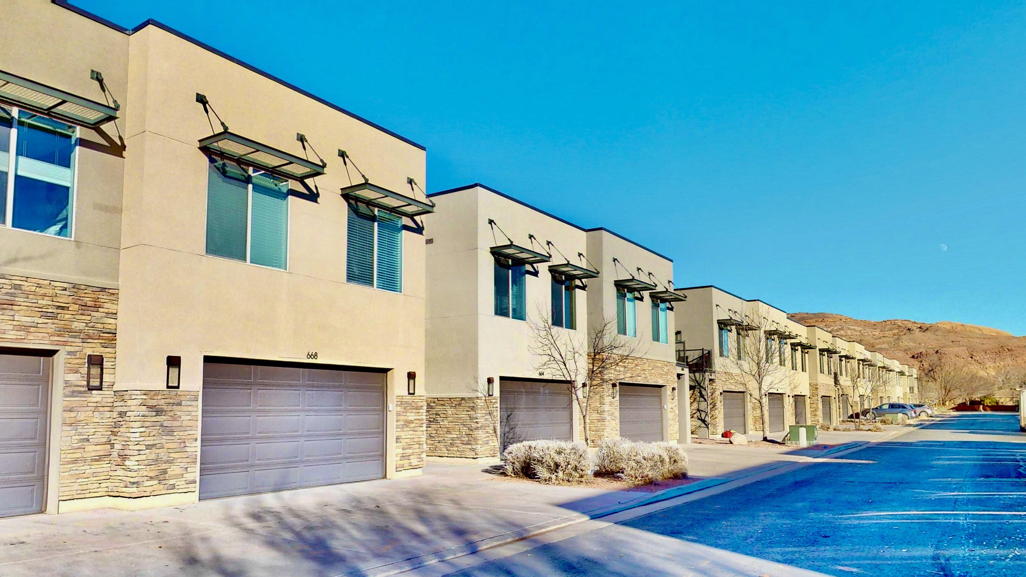 Modern stucco exterior with stone veneer accents, individual garage doors, and contemporary window awnings