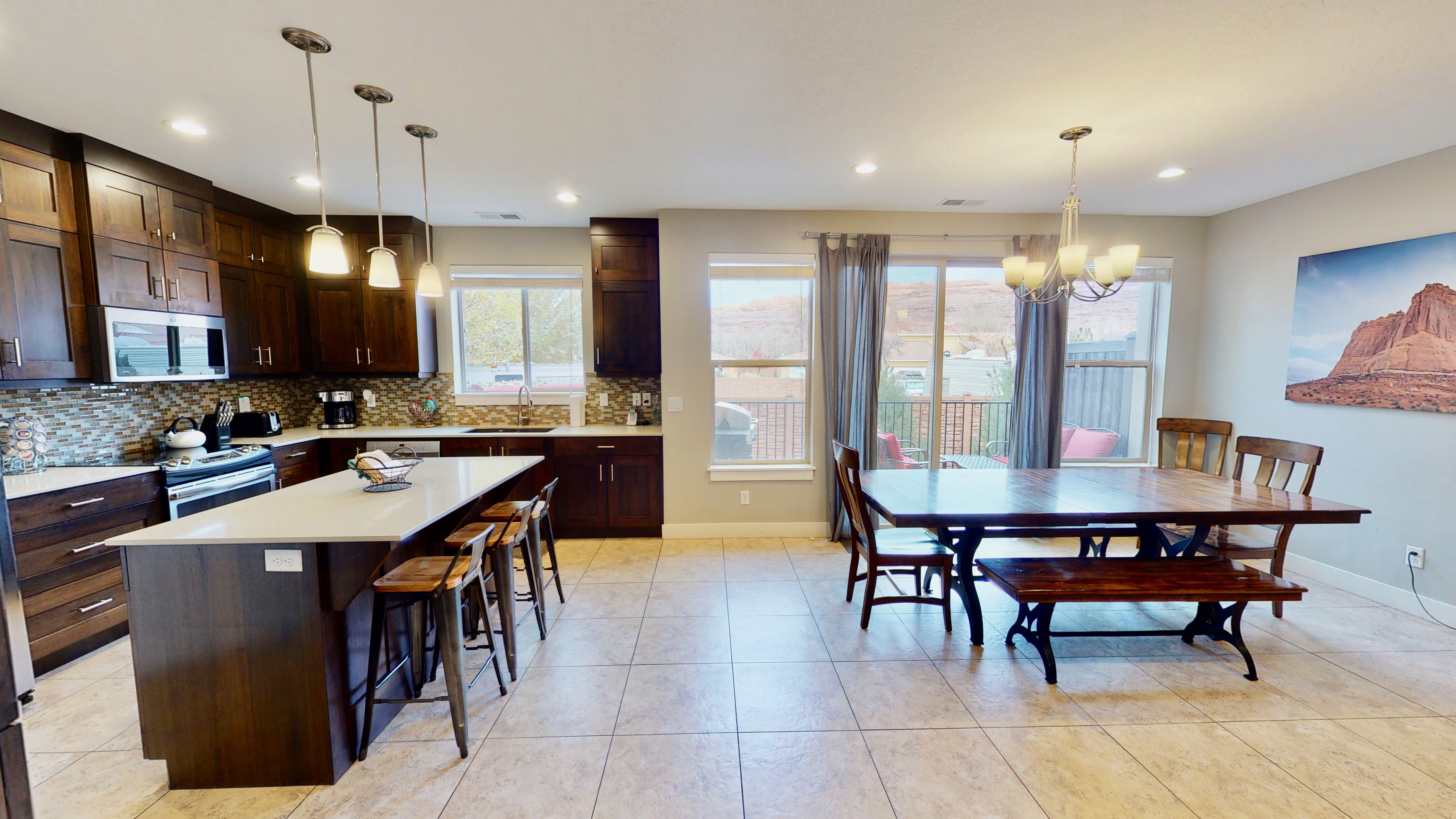 Kitchen and dining area featuring dark wood-finish cabinetry, a large kitchen island with pendant lighting, a tile backsplash, stainless steel appliances, and tile flooring