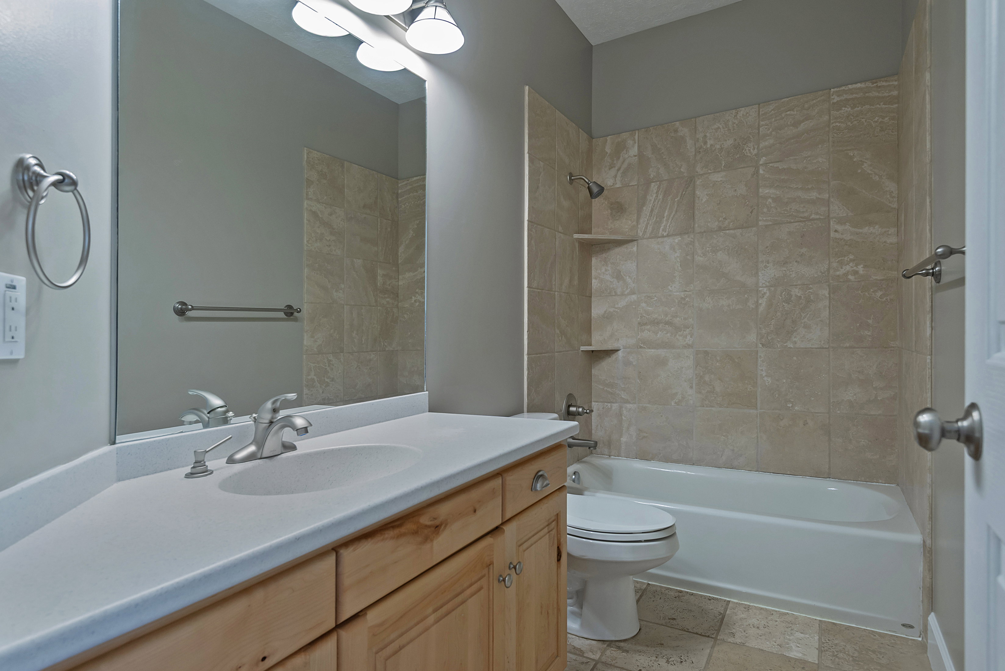 Bathroom featuring a wood-finish vanity with an integrated sink, a full-width mirror, and a tiled shower/tub combination with built-in shelving