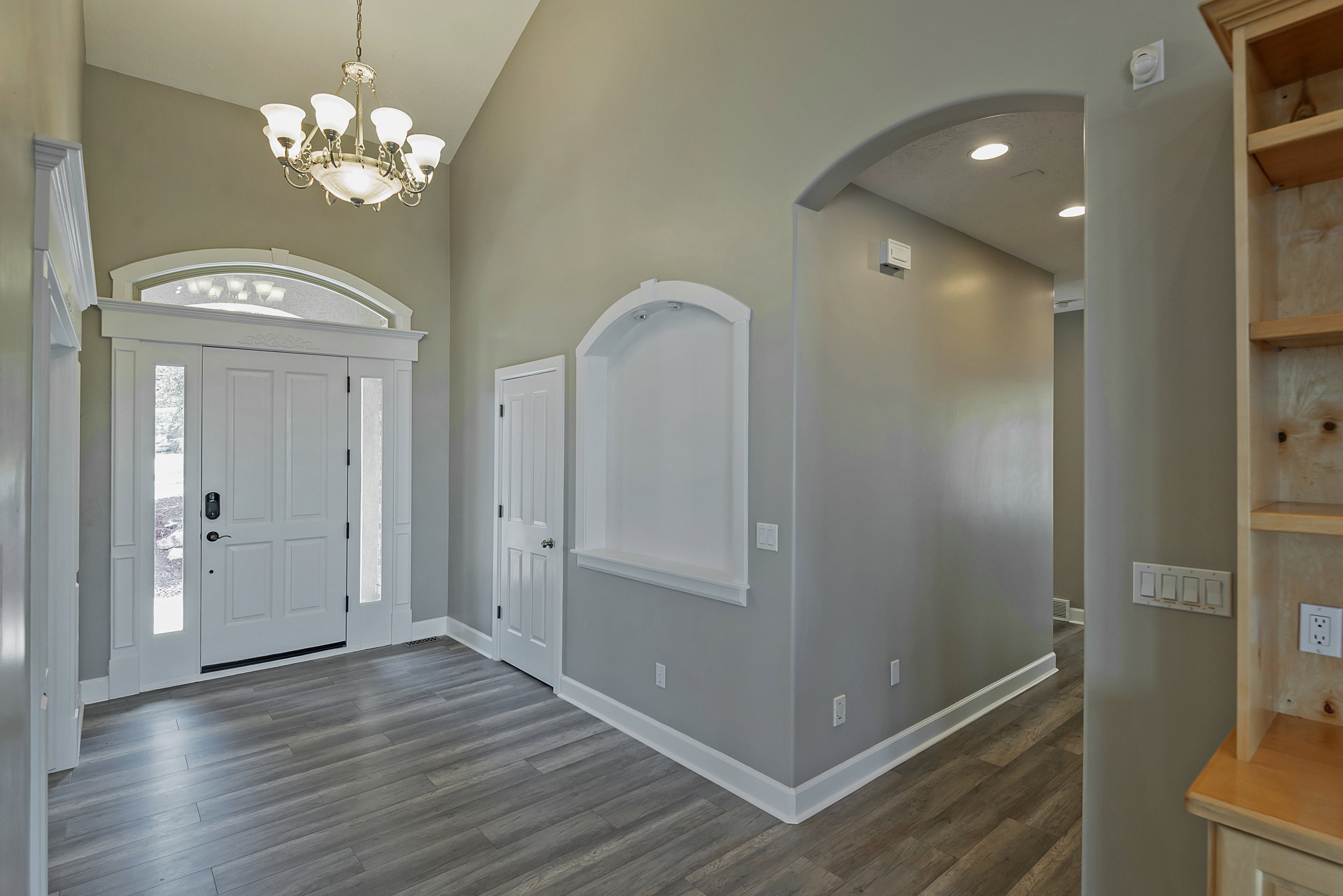 Entryway featuring a decorative transom and sidelights flanking the main door, wood-finish flooring, a contemporary chandelier, an arched wall niche, and an arched hallway opening